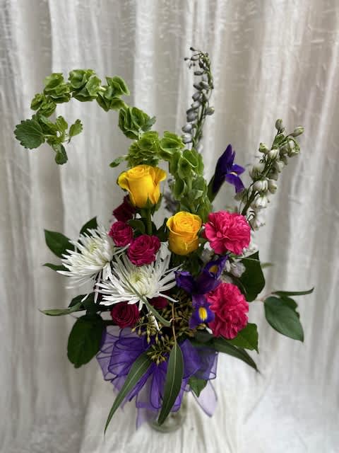The Happy Mama - This Beautiful arrangement combines lavender delphinium, bells of Ireland, Iris, carnations, spray roses, mums and roses to create a breath taking gift the mom in your life is sure to love.