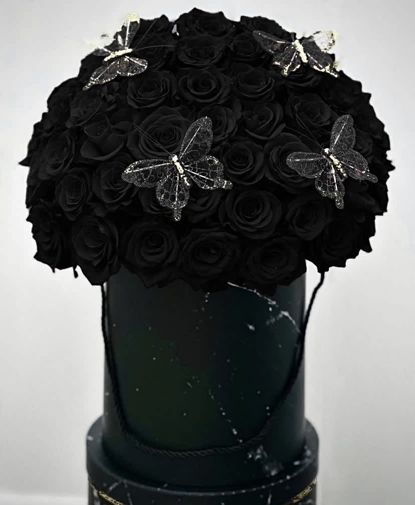 Black Butterfly - A stunning black box adorned with 50 elegant black roses, each petal a midnight whisper against the purity of the box. Delicate gold butterflies dance around the arrangement, their iridescent wings adding an ethereal touch to the scene. Atop the bed of roses sits a regal crown, casting a royal aura over the entire composition, as if bestowing majesty upon the blossoms below. 