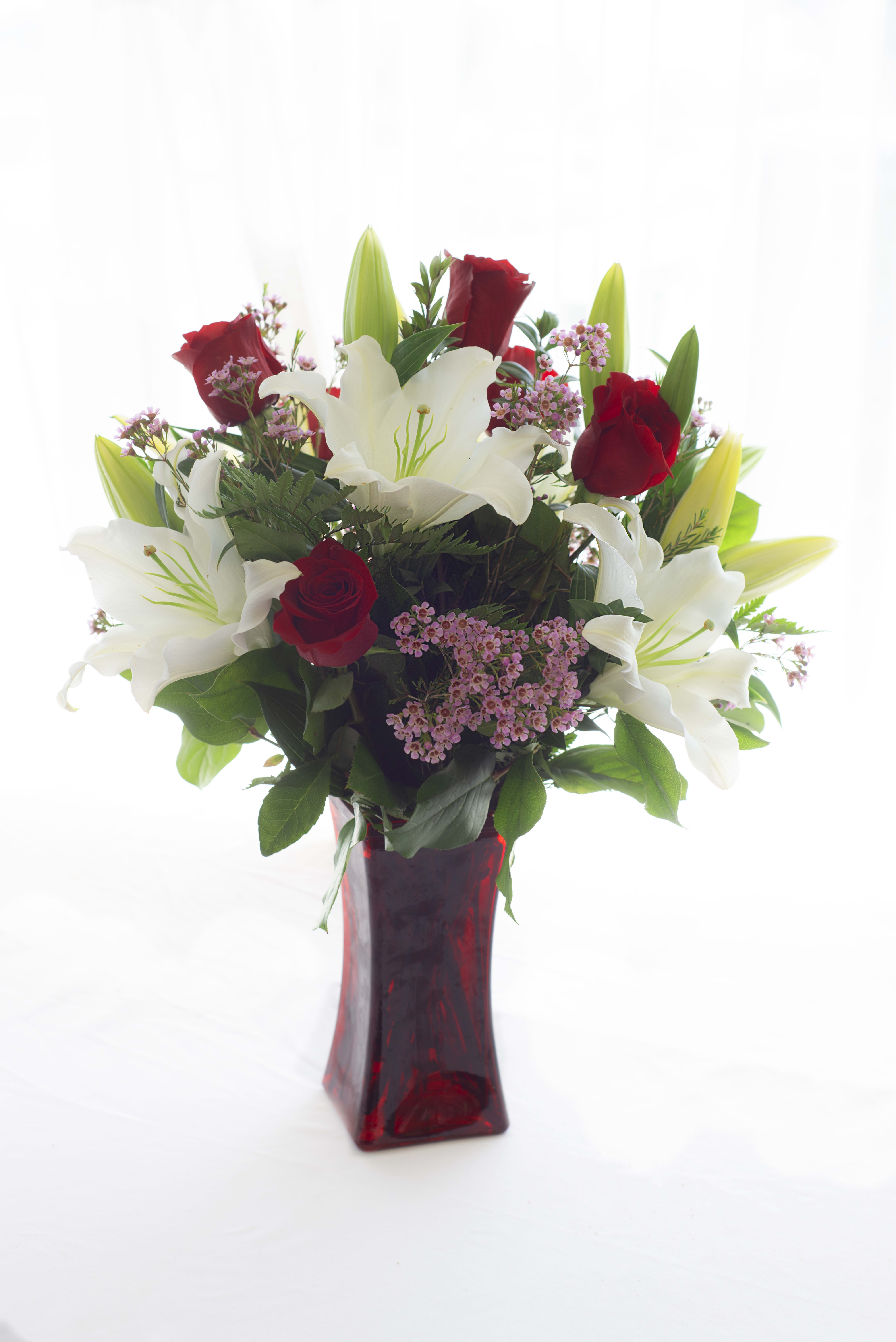 Lilies and Roses Oh My! Lilies and Roses Oh My! - 6 Red Roses and White Oriental Lilies accented with pink wax flower and beautiful greens in a colored vase.