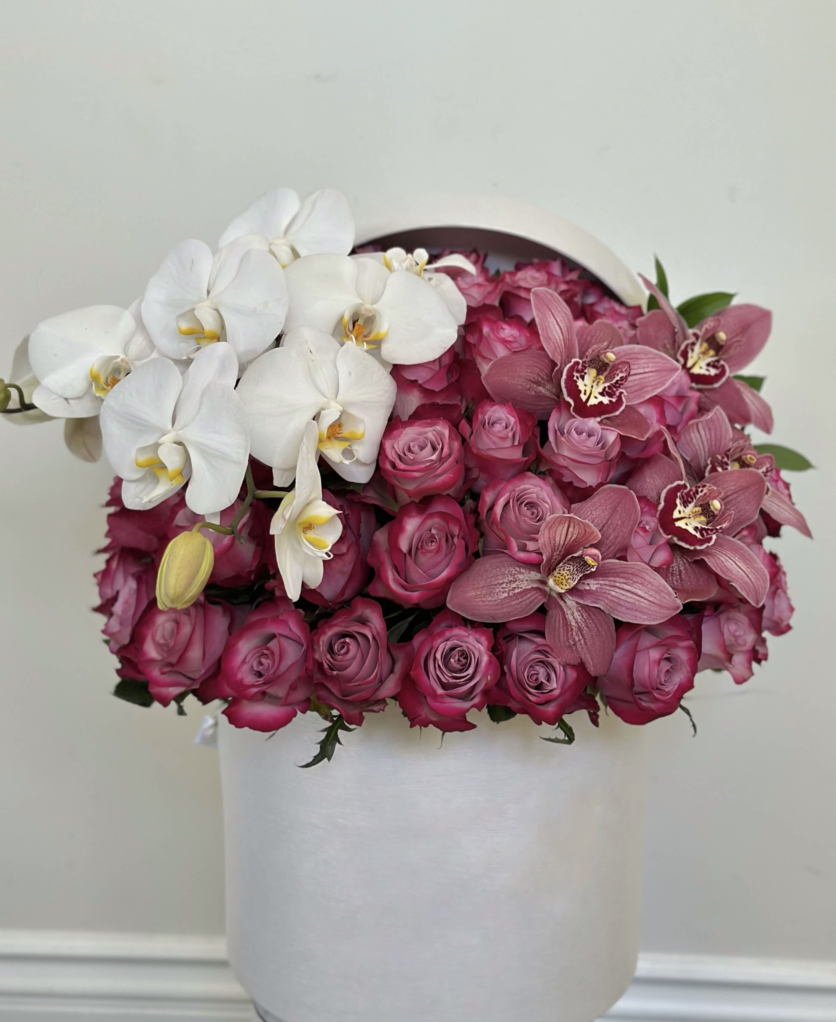 Elegant Box  - In a pristine white box, a harmonious tapestry of beauty unfolds. Soft pink roses, their petals delicately unfurling like whispers of love, infuse the arrangement with a sense of romance and tenderness. Nestled among them, orchids bloom in hues of blush and ivory, their ethereal elegance adding a touch of mystique. Standing out amidst this floral symphony, a cymbidium orchid boasts velvety petals in a captivating shade, commanding attention with its regal presence. Together, they create an enchanting tableau, a testament to the timeless allure of nature's artistry. 