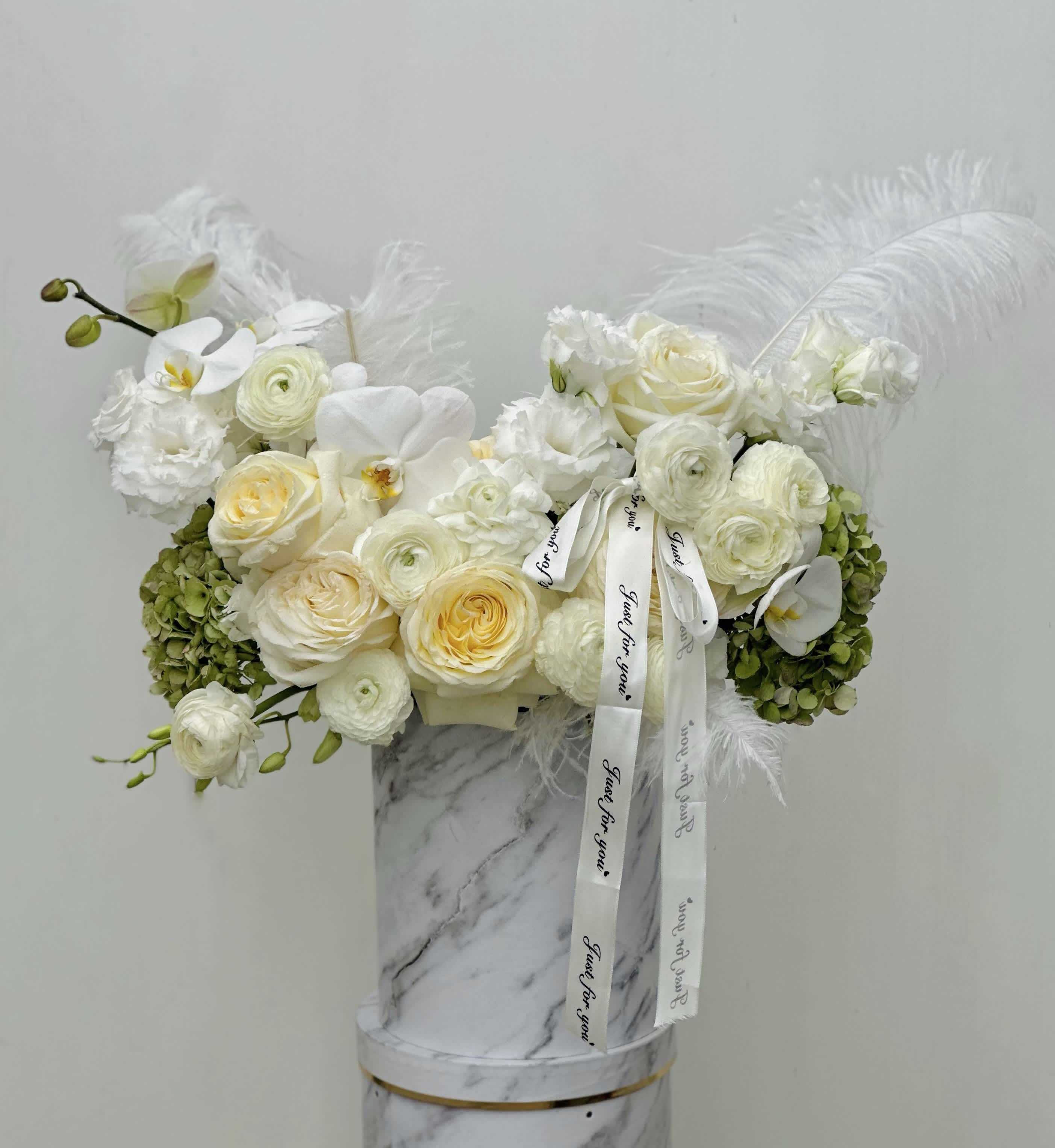 Flower Wings - In a pristine white box, a bouquet of pure enchantment blossoms. Roses, their petals soft as whispers, exude romance and grace, while orchids add an exotic allure with their delicate blooms. Amidst this tapestry of beauty, ranunculus blooms burst forth in vibrant hues, their layers of petals resembling delicate silk. Intertwining with elegance, amaranthus cascades gracefully, adding a touch of whimsy and movement. Completing this symphony of botanical wonder, anthurium blooms stand tall with their vibrant, heart-shaped petals, radiating passion and charm. Together, they create a mesmerizing tableau, a celebration of nature's artistry that enchants the senses and lifts the spirit.