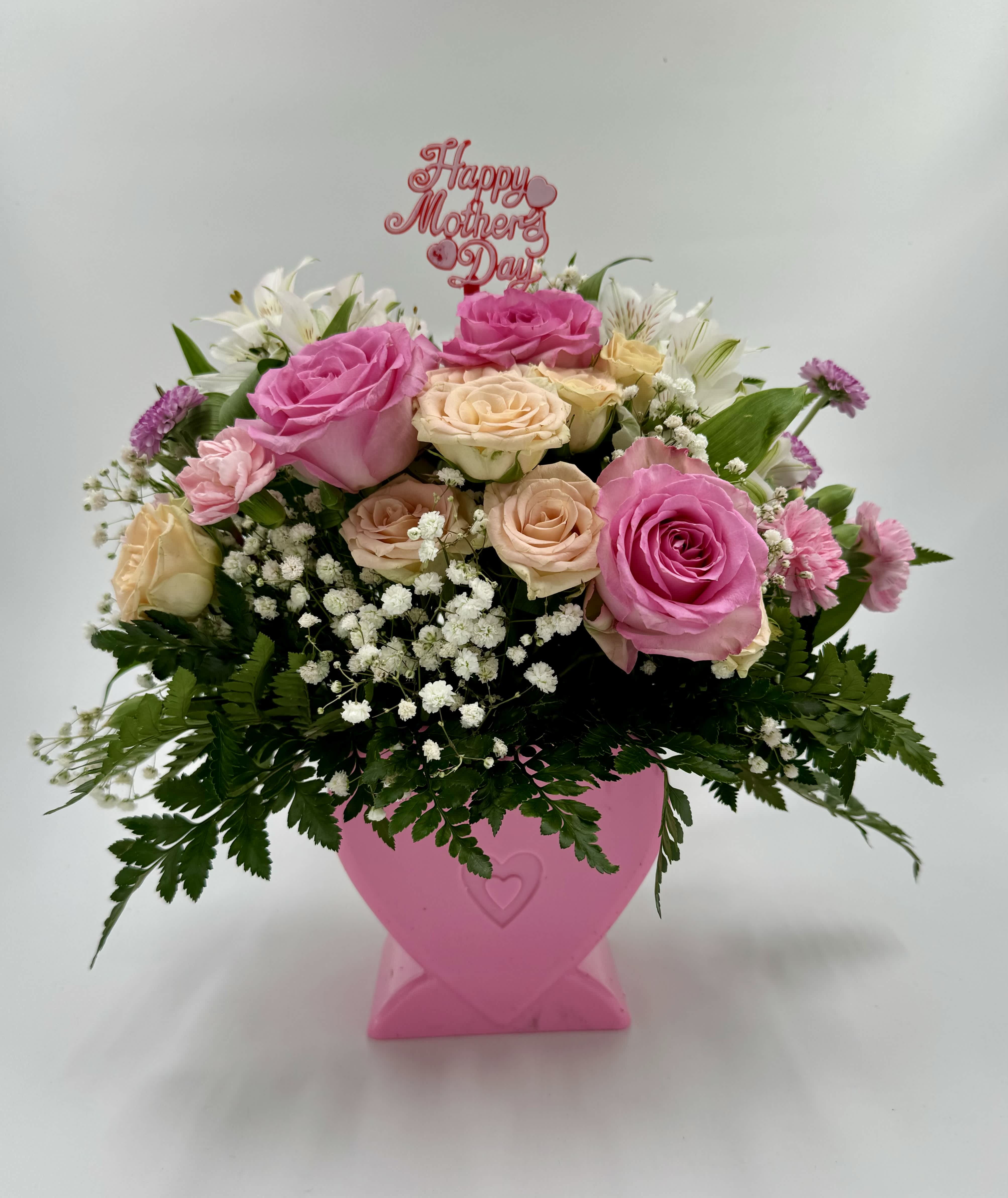 Jardín de Amor Maternal - This arrangement consists of 3 pink roses, 7 peach-colored roses, baby's breath, carnations, and leather leaf. It comes in a heart-shaped plastic vase in pink.