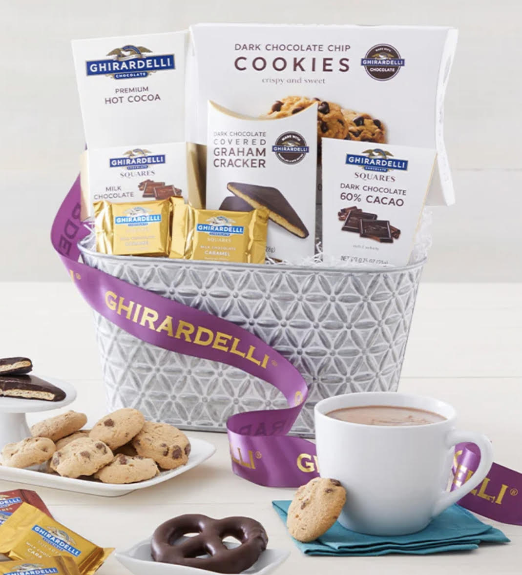 Classic Ghirardelli Gift Basket - Share an abundant gift basket filled with some of Ghiardelli’s best. Finished with a beautiful ribbon, each embossed silver metal basket is brimming with classics like rich chocolate chip cookies, smooth hot cocoa mix, and decadent chocolate squares. Choose from the Deluxe, Grande, and Supreme options for an increasingly indulgent chocolate assortment designed to impress.  