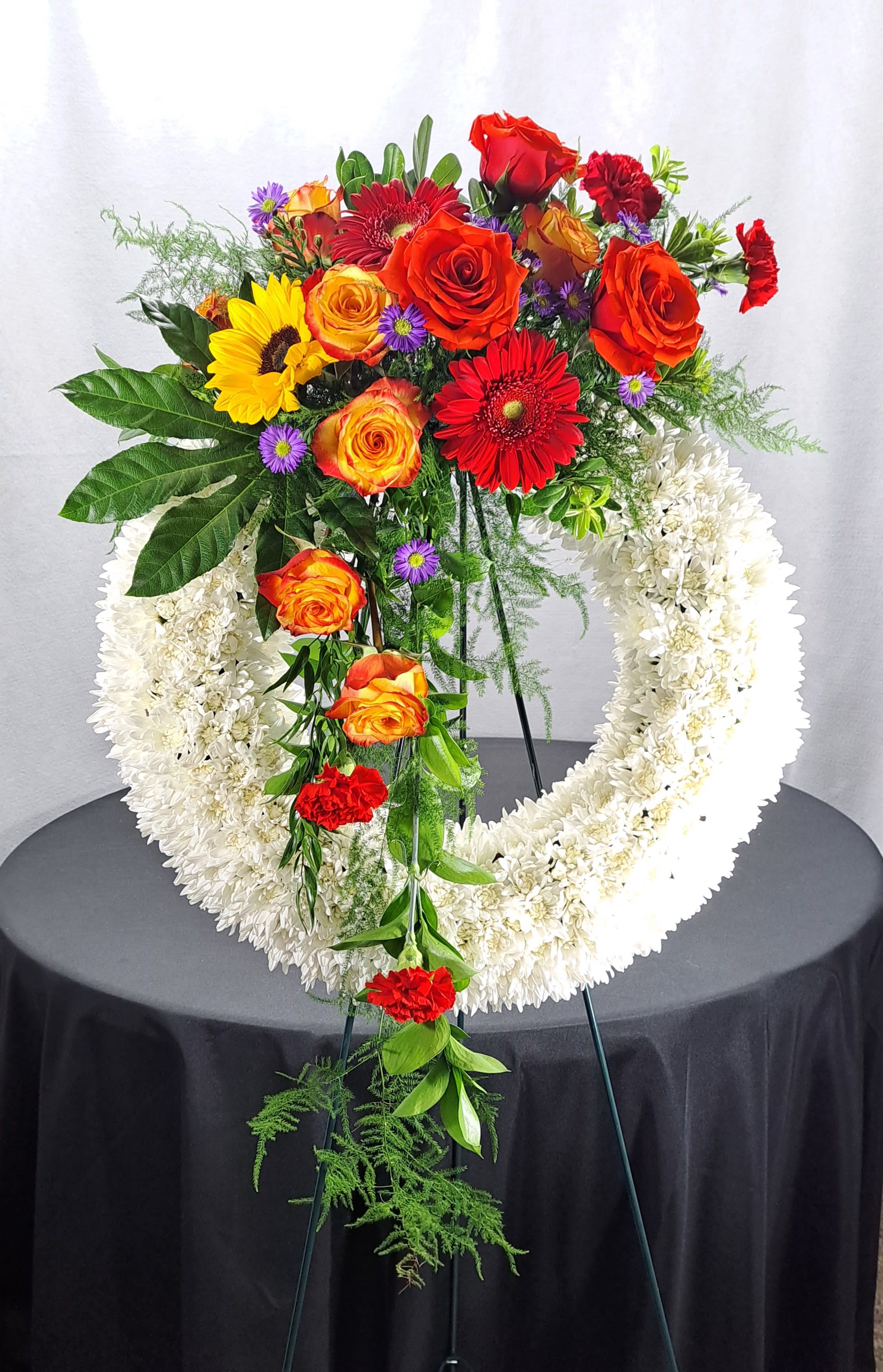 Mixed-Color Sympathy Wreath Standing Spray by ABM Floral Studio - Gerbera Daisies, Carnations, Chrysanthemums, Roses, Sunflowers, Aspidistra Leaves, and Plumosa Leaves 22&quot; diameter Wreath Standing Spray.