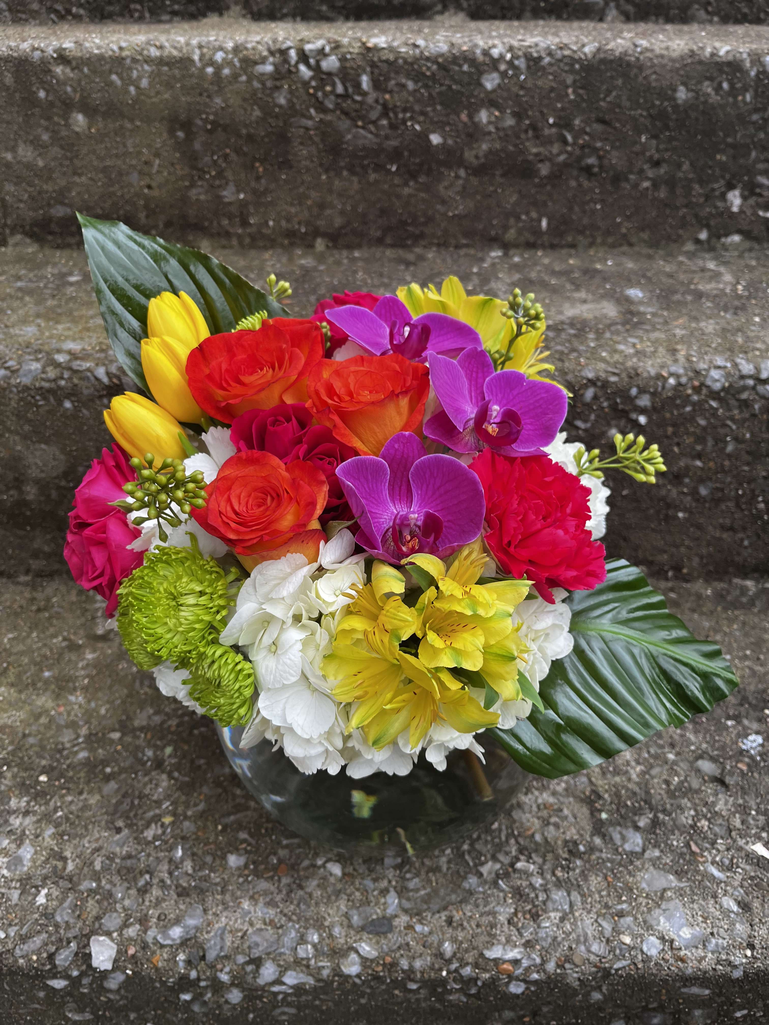 Tropical Day Dream - This arrangement has three orchid flowers, hydrangeas, alstroemeria, roses, tulips, spray roses, buttons, carnations, and beautiful greenery. The Orchid color may be changed based on availability.