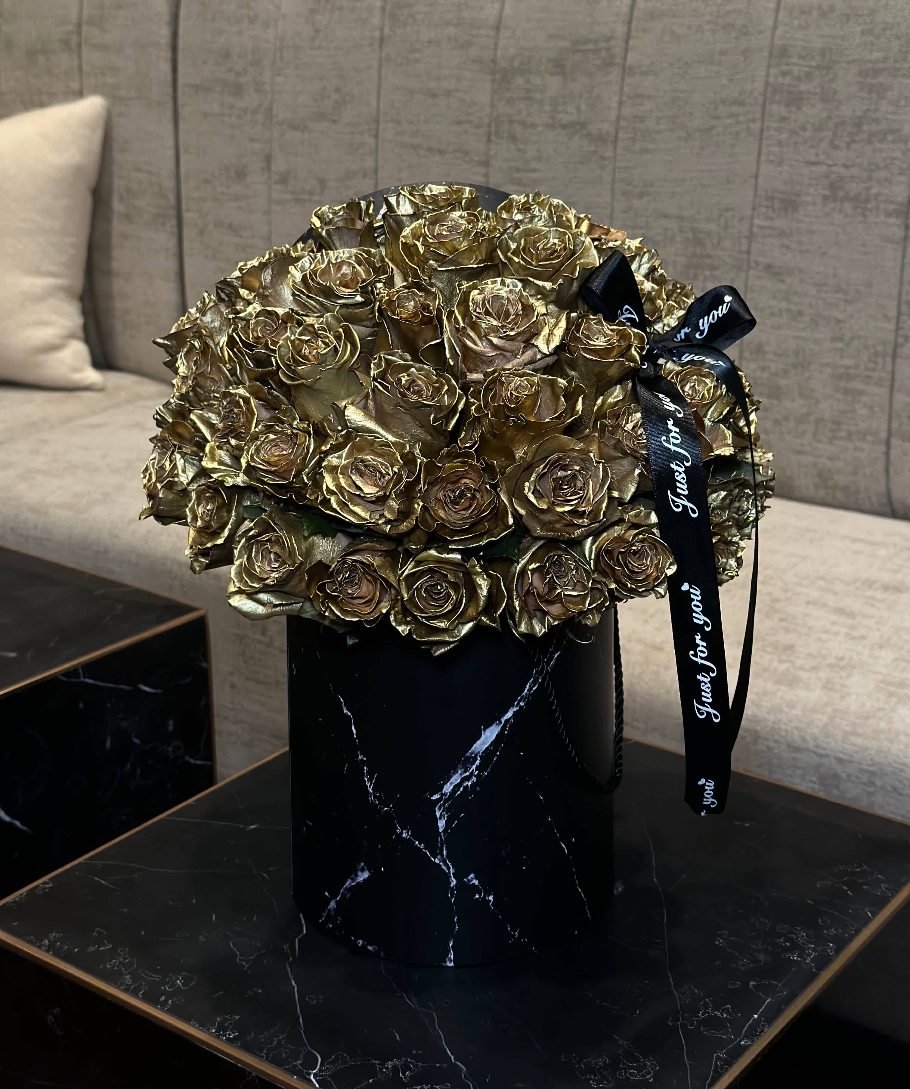 Golden Roses in a Black Box - Within the depths of a sleek black box adorned with a glistening golden bow lies a treasure of opulence - golden roses, resplendent in their grandeur, exude an aura of regal elegance. Each bloom, a symbol of luxury and sophistication, delicately nestled amidst the velvety darkness, promising a journey into the realm of timeless allure and refined beauty. 