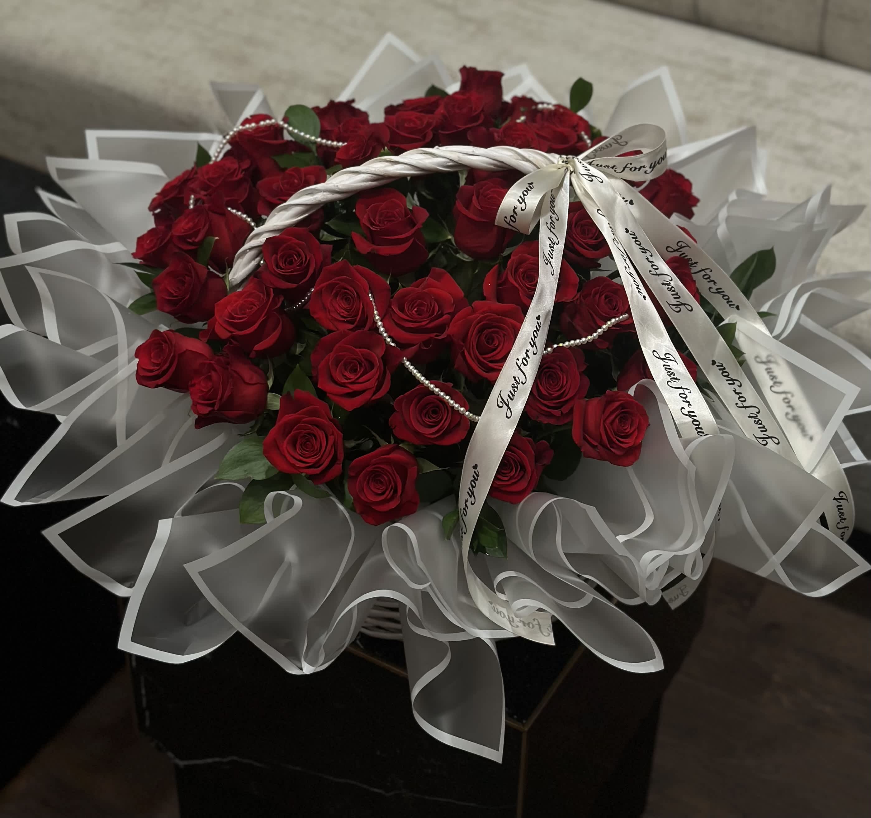 Basket with Red Roses - A white basket, akin to a gown for the most delicate dreams, crowns the beauty of red roses, like drops of passion scattered across a snowy canvas. And the shimmering beads, like pearls of morning dew, lend an incomparable charm to the ensemble, magically framing this masterpiece of nature.