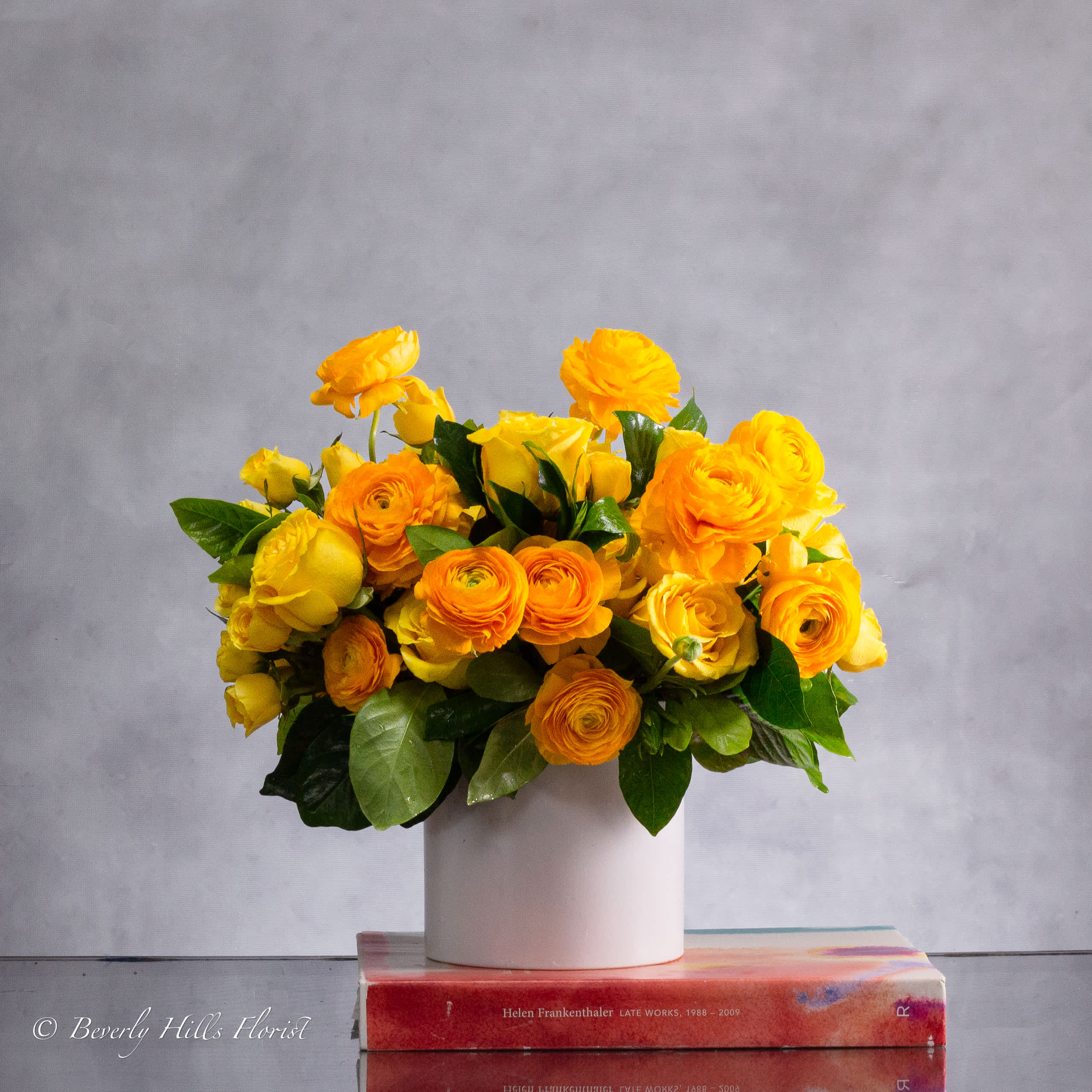 GOLDEN FLOWERS - Brighten someone's day with our Sunshine Serenade Bouquet, featuring a stunning blend of vibrant yellow roses and delicate yellow ranunculus. Each bloom is carefully selected for its freshness and beauty, creating a harmonious arrangement that exudes warmth and joy.  The cheerful yellow roses symbolize friendship and happiness, while the charming ranunculus adds layers of elegance and sophistication. Expertly arranged in a lush, rounded bouquet, this arrangement is perfect for any occasion, whether you're celebrating a birthday, anniversary, or simply want to brighten someone's day.  Let this radiant bouquet spread sunshine and smiles wherever it goes!  Standard AS Shown one Dozen Roses with other seasonal Flowers   Deluxe 2 Dozen Roses with other seasonal Flowers  Deluxe 3 Dozen Roses with other seasonal Flowers   about 11&quot; Round 