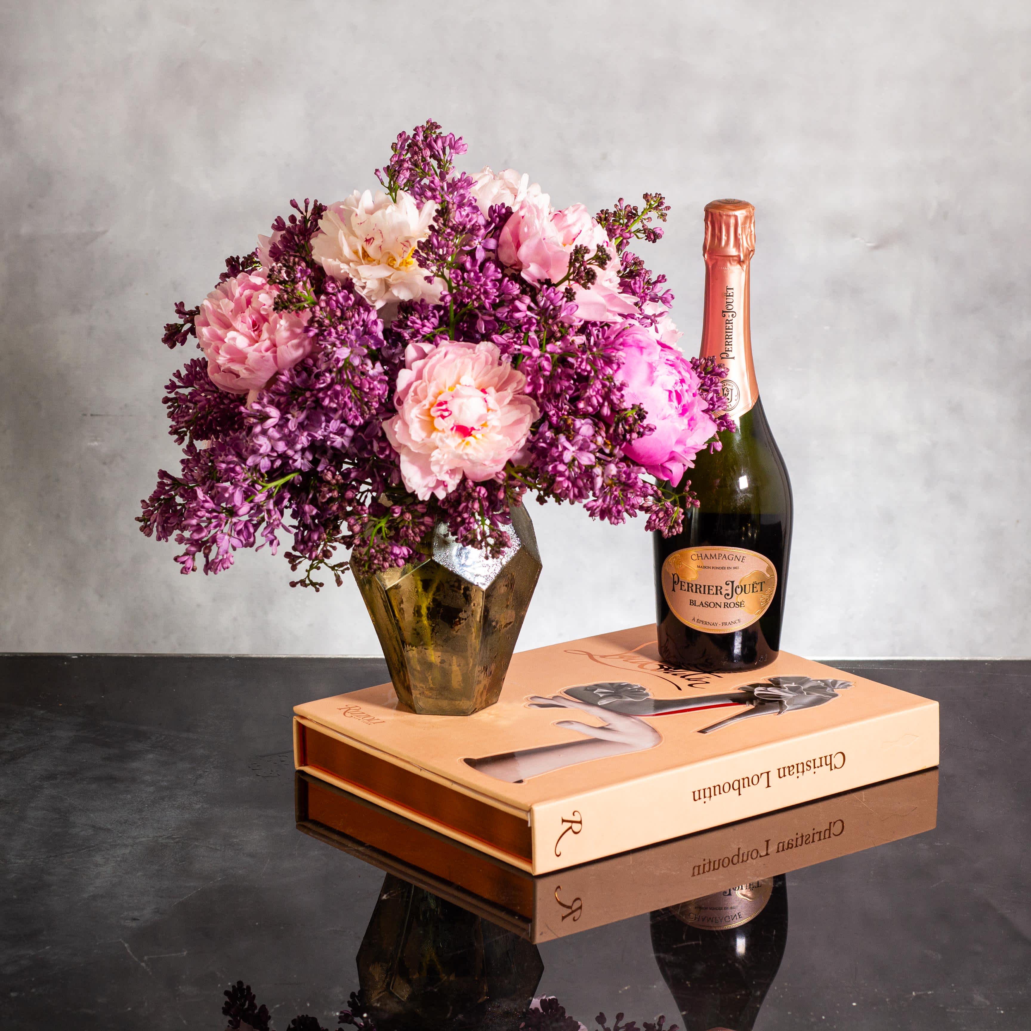 Blushing Skies - A Cinematic Journey - The beautiful arrangement features blush color peonies and purple lilacs gathered together in a diamond-shaped amber-colored modern vase. Standing at 6 inches in height and 9 inches in width, the overall height of the arrangement is 12 inches. This modern and elegant display is available for same-day delivery in Beverly Hills and Los Angeles, perfect for adding a touch of sophistication and beauty to any space.