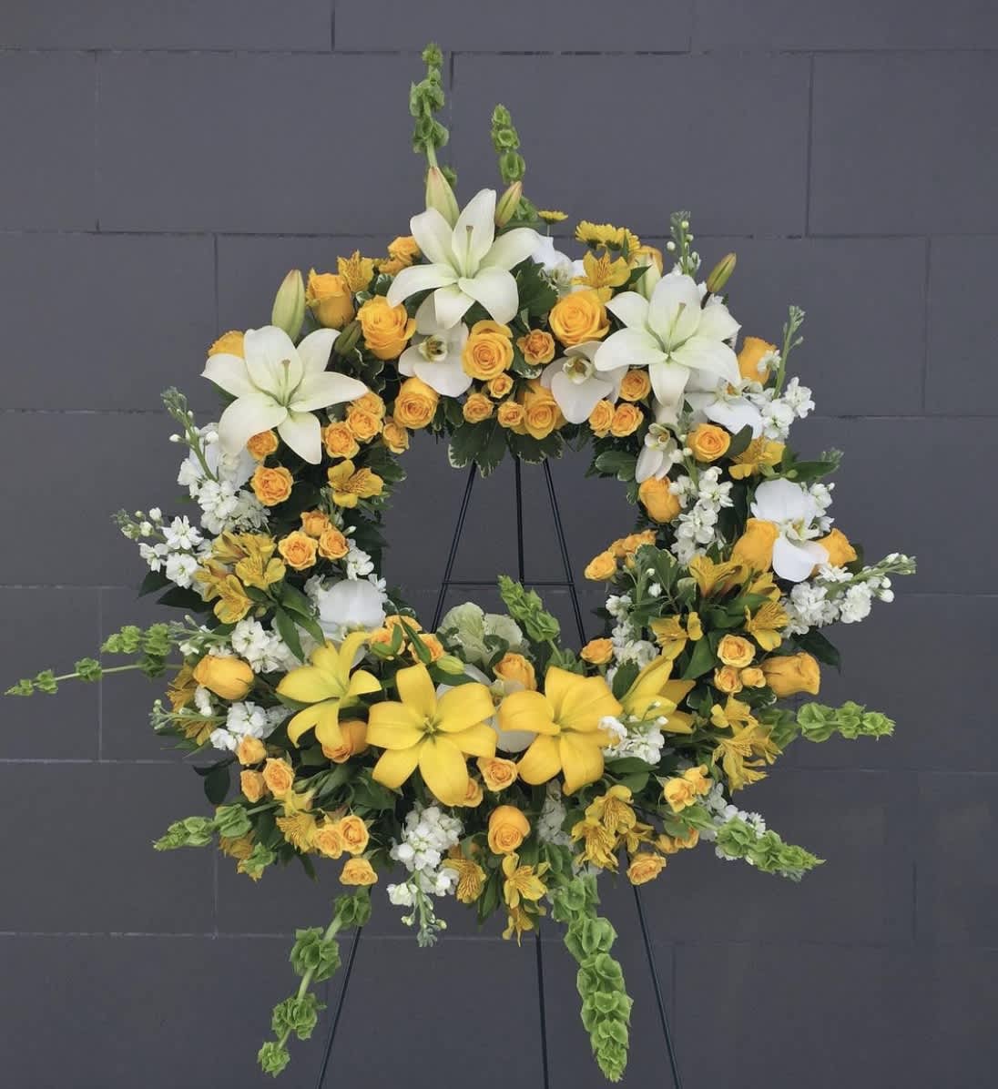 Warm Company - Beautiful yellow and white funeral wreath featuring lilies, roses, stock, sunflowers, and green accents.