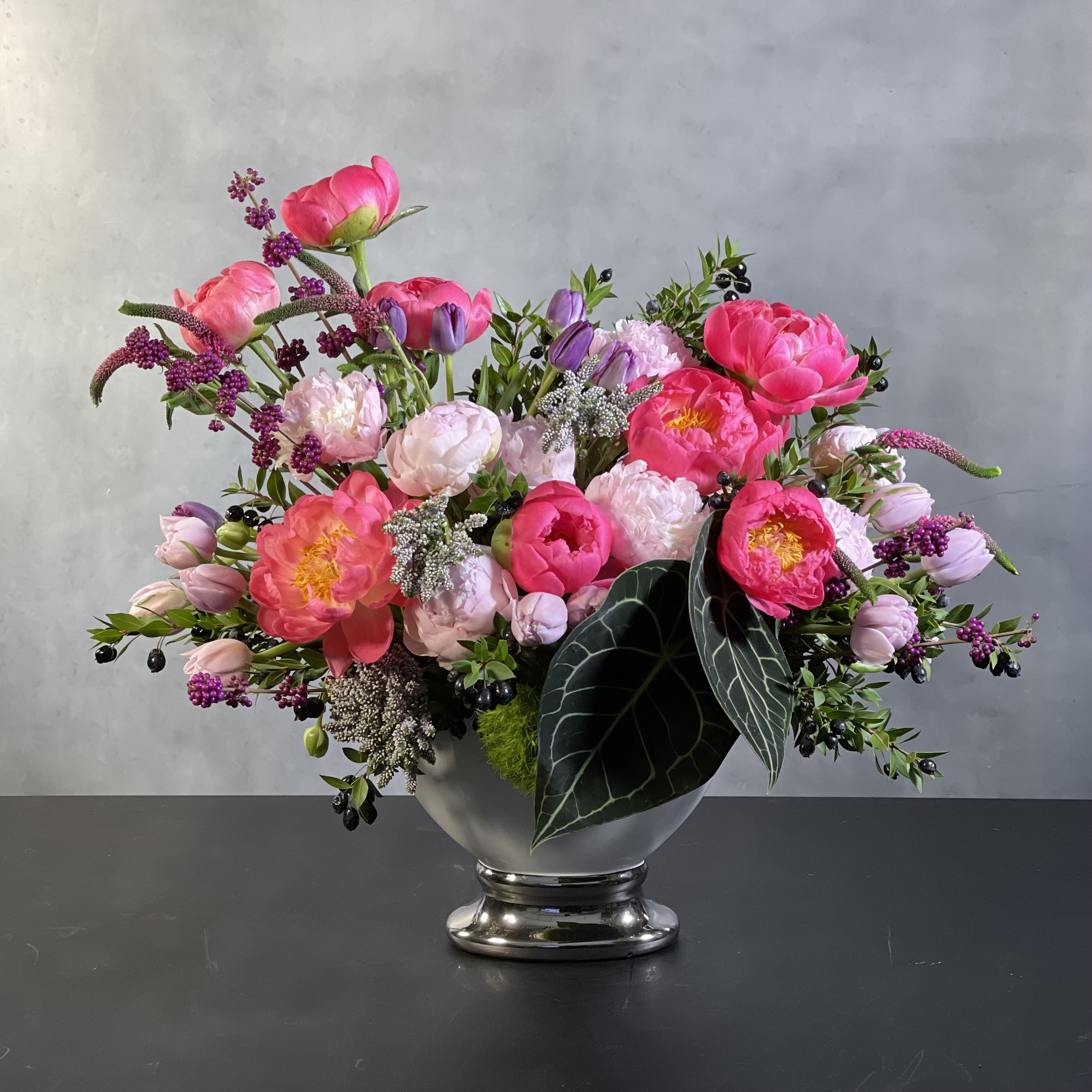 specially for you.  - A cheerfully elegant piece that is sure to be a statement in any room that it is placed in. Adding a beautiful touch of color and brightness to keep its surroundings fresh. In this arrangement there is a balance of Peonies, Tulips, Seasonal Berries and Tropical Leaves .  Container may Vary. 