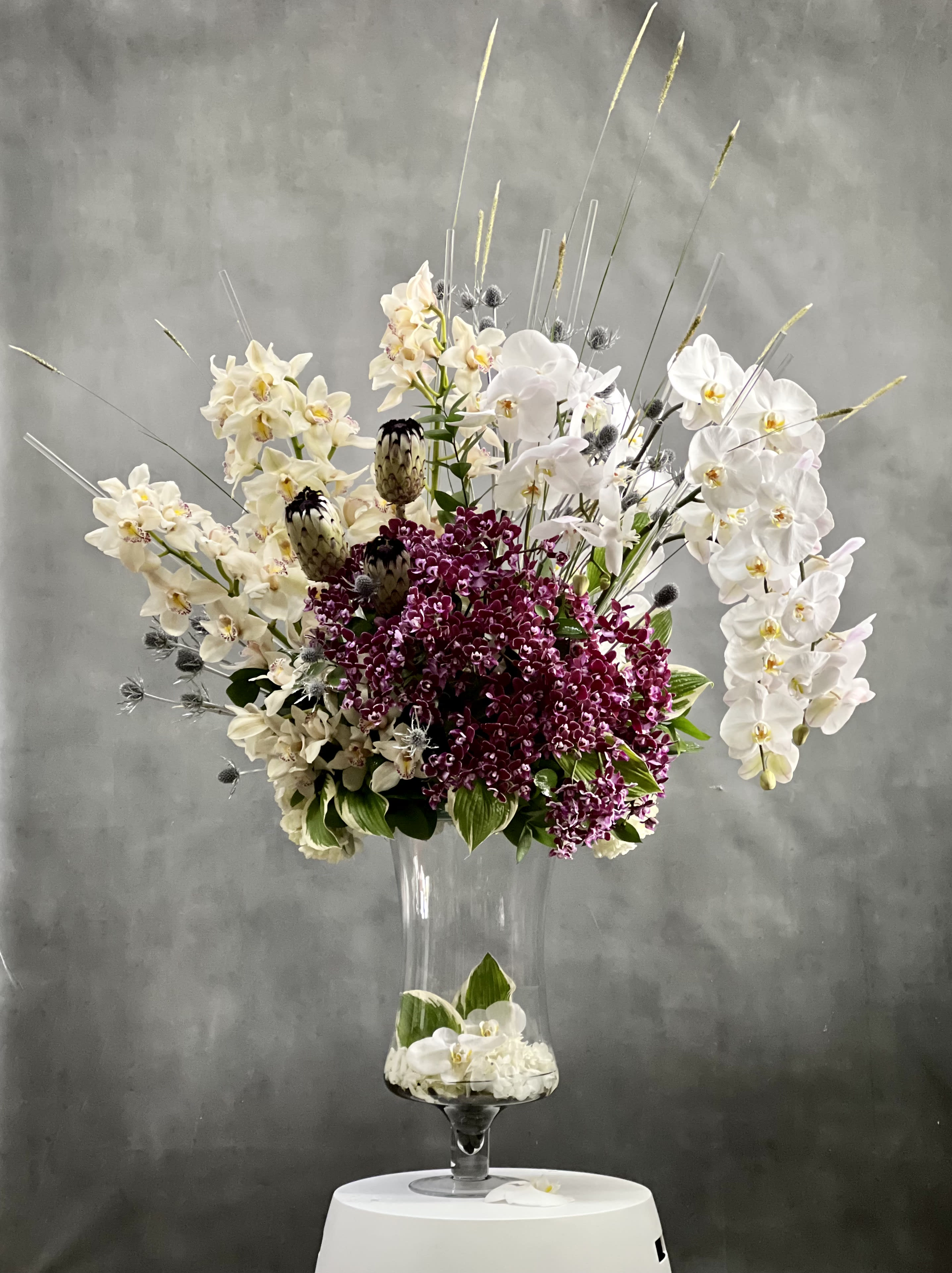 Designers Choice - Grand Orchid Bliss - Overflowing of assorted Orchids artfully arranged in tall pedestal vase. This is an ideal choice for someone who deserves an over the top floral. It is a statement piece for any setting.