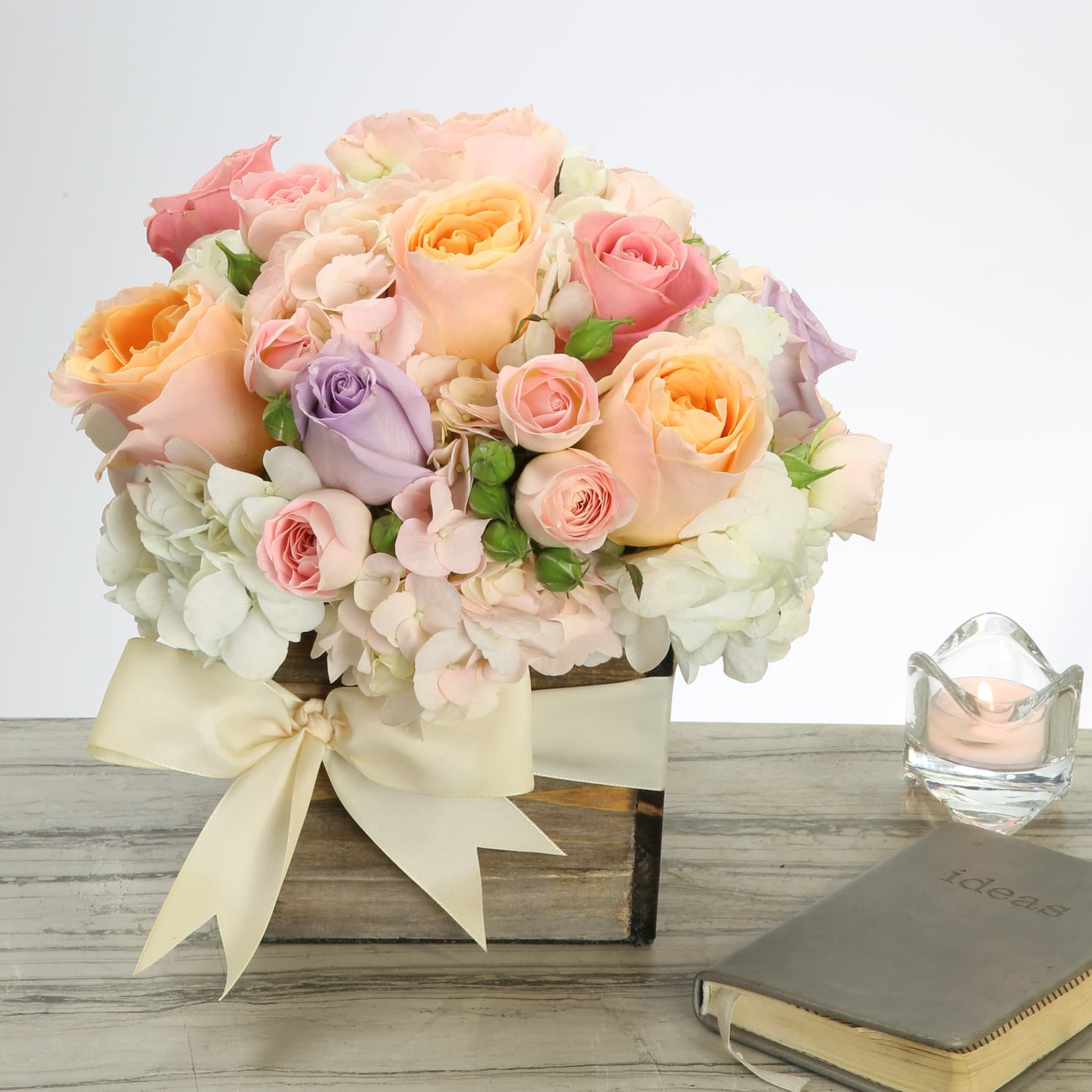 Pastel Perfection - Soft luscious pastel South American roses, embraced by Dutch Hydrangeas and a sprinkling of seasonal flowers make this delightful design one of calm and fragrant beauty. The custom bow tied around the box base puts the finishing touch on this lovely arrangement that will have everyone saying OMG!  Standard: Approx. 8"  in a 6 X 6 Container Deluxe: Approx. 12" in a 6 X 6 Container Premium: Approx. 16" in a 8 X 8 Container
