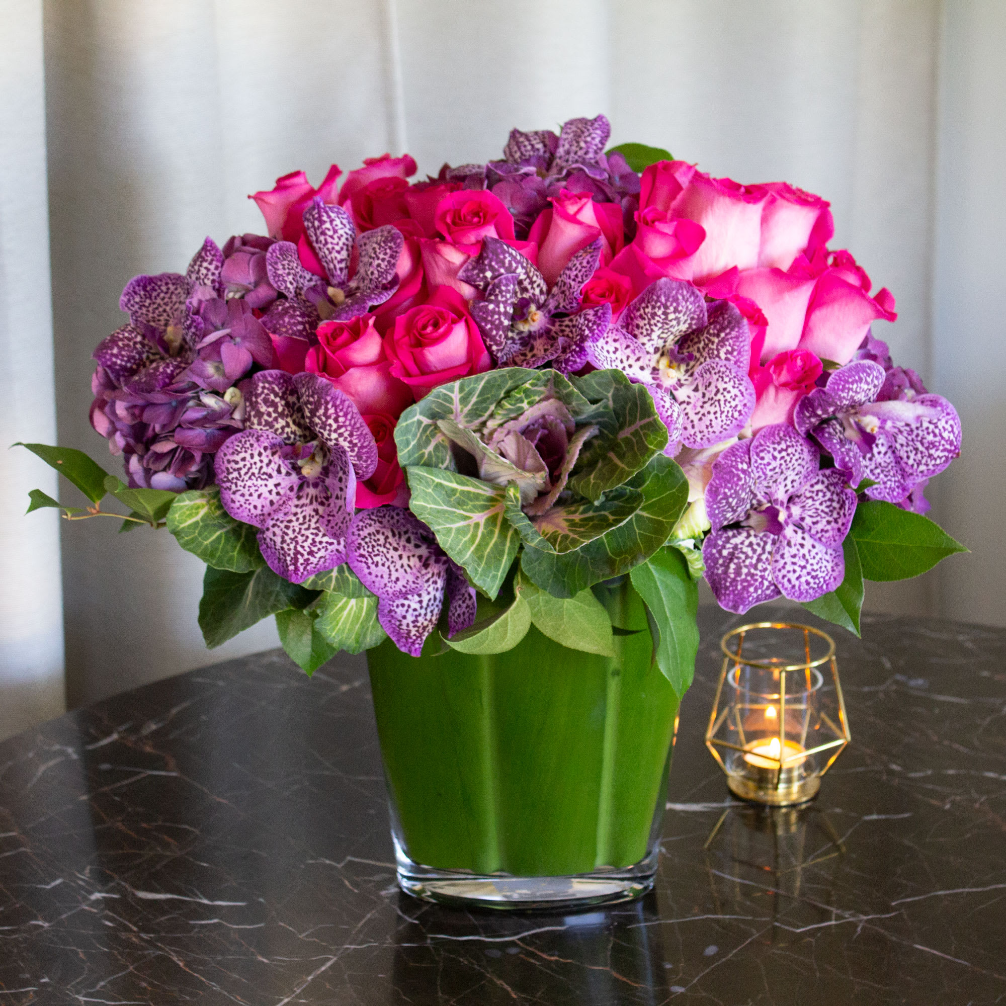 Floral Bliss Floral Bliss - Pink and purple blooms are a sweet and innocent way to show your affection. Floral Bliss features a leaf-lined glass vase bursting with pink Carrousel Roses, purple speckled Vanda Orchids, purple Hydrangeas with touch of green kale. This chic bouquet of feminine colors is full of texture and makes a fabulous gift. Approx: 19" H Standard as shown Deluxe: Features 50 Roses & additional Orchids Premium: Features 100 roses & additional Orchids