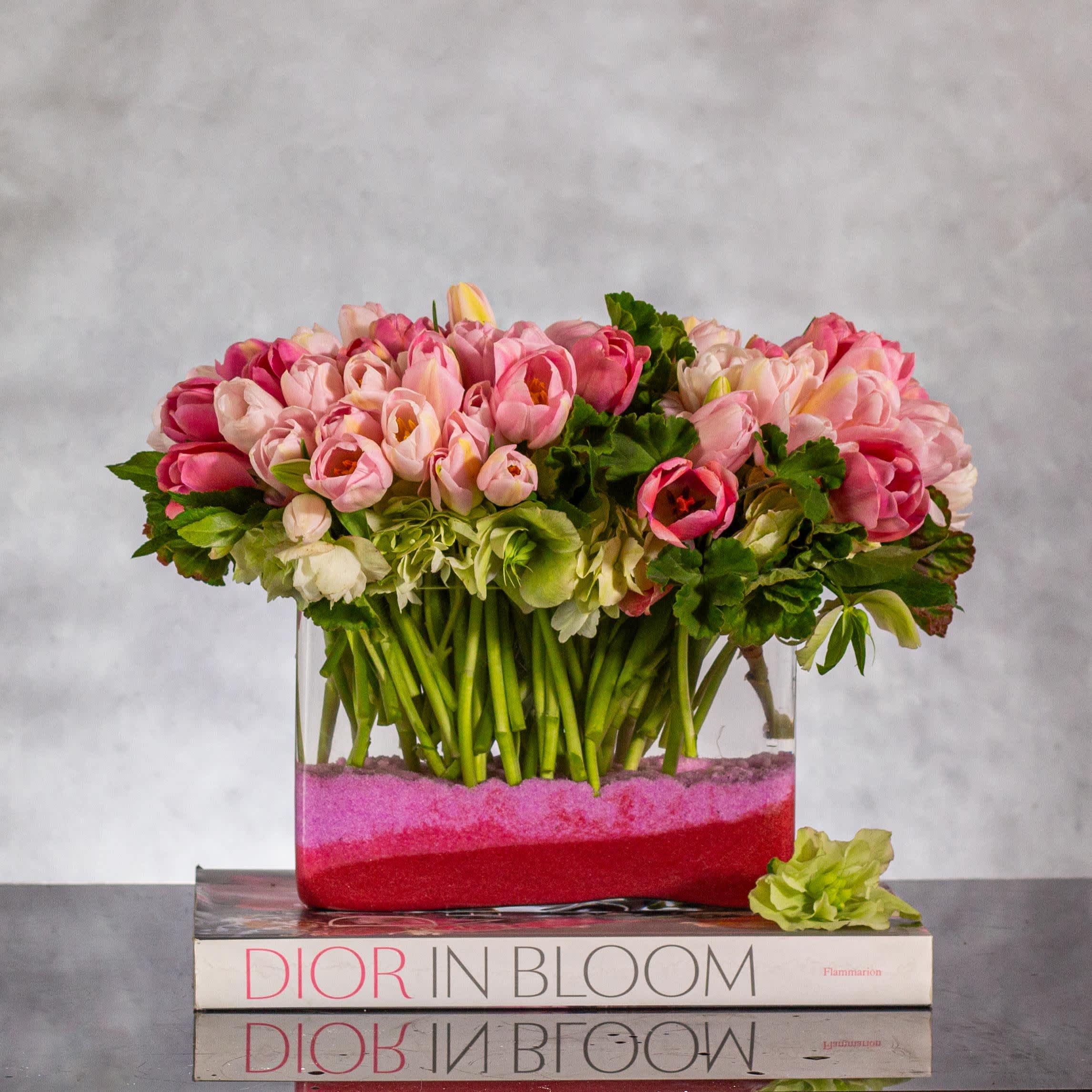 Pink Elegance - Over 80 Tulip Floral Arrangement - Same-day delivery: Embrace the essence of sophistication and beauty with our exquisite floral arrangement showcasing over 80 pink tulips. Pink tulips symbolize affection, care, and admiration, making them a perfect choice to convey heartfelt emotions. Carefully arranged in a rectangular vase measuring 9 inches in length and six inches in height, this display exudes elegance and charm. Adorned with sand for an extra touch of grace, this arrangement stands at an overall height of 10 inches, adding a luxurious touch to any space.  Ideal for any occasion, from birthdays to celebrations of love, our tulip arrangement is a true showstopper. With our reliable same-day delivery service, you can surprise your loved ones with this floral masterpiece, carrying profound messages of love and appreciation. Brighten someone's day with a gift that not only embodies beauty but also speaks volumes of heartfelt sentiment.