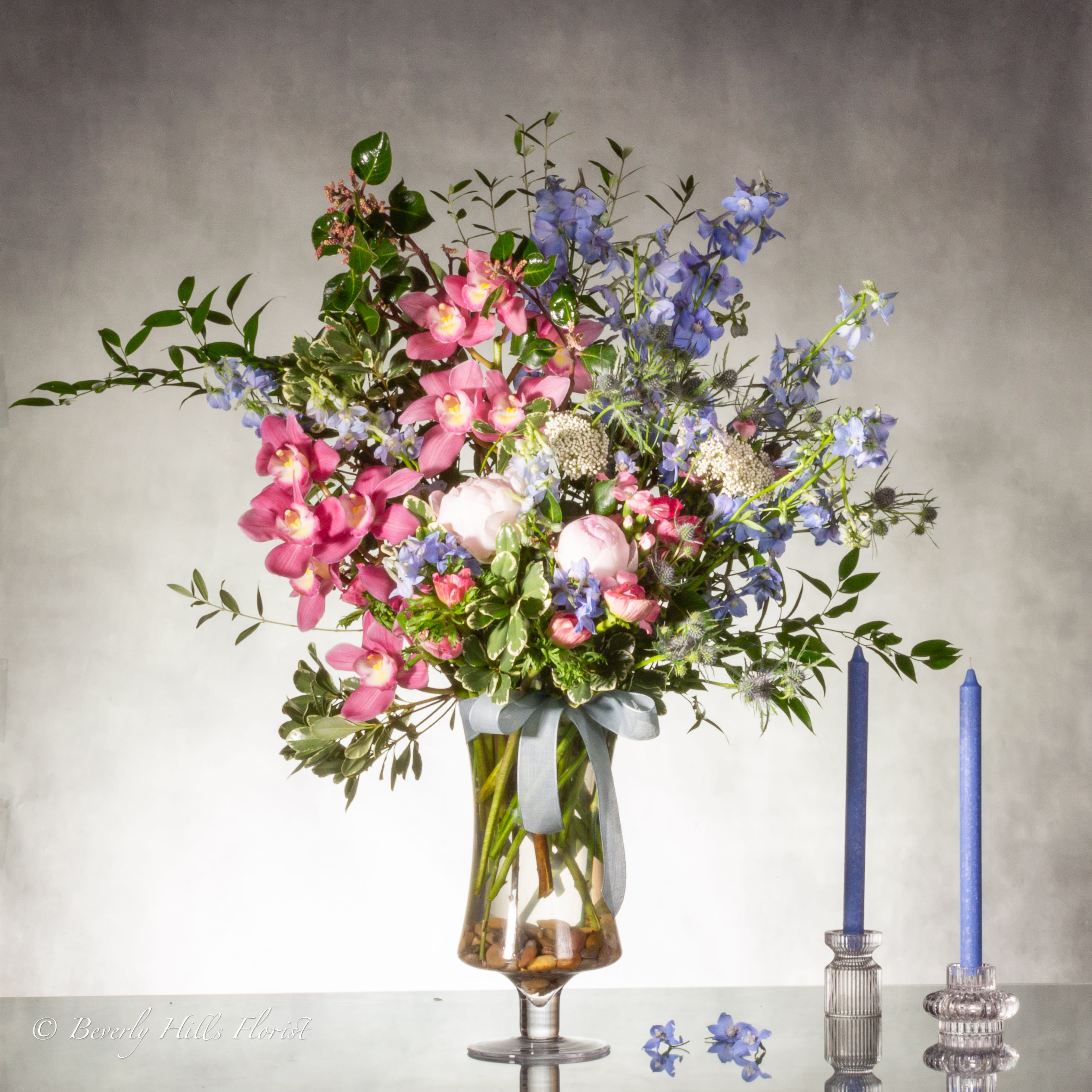 A Floral Tale of Love and Beauty - Beverly Hills Florist presents the &quot;Grand Look&quot; in floral artistry with this arrangement. The combination of pink orchids and delphiniums in the tall glass vase exudes a sense of grandeur and opulence. It's the perfect choice when you want to make a grand statement or create a memorable focal point at any special occasion.  AS SHOWN - DELUXE 