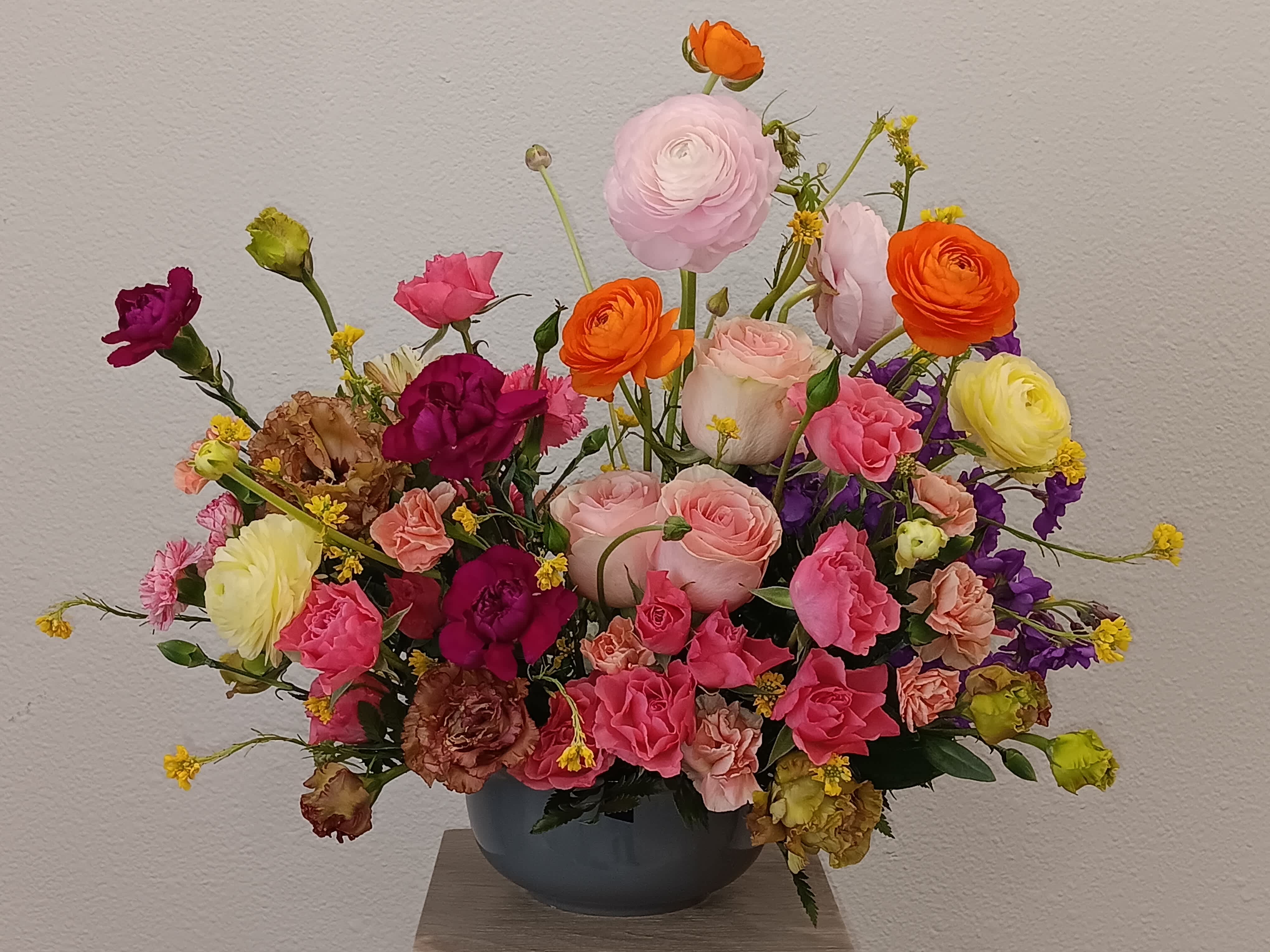 in Style  - Express your love with the eloquence of Shakespeare - without saying a word. She'll adore this exquisite bouquet of roses and ranunculus and other pastel favorites in a classic ginger vase. And she'll know just the words to let you know. Light pink roses, pink, yellow and orange ranunculus, purple stock, gold lisianthus, pink and hot pink spray roses are mixed with variegated pittosporum in a ceramic vase. Orientation: All-Around  SUBSTITUTION POLICY – Always deliver the freshest flowers! Please note the bouquet pictured reflects our original design.  If the exact flowers or container in this arrangement are not available, our local florists will create a beautiful bouquet with the freshest available flowers.