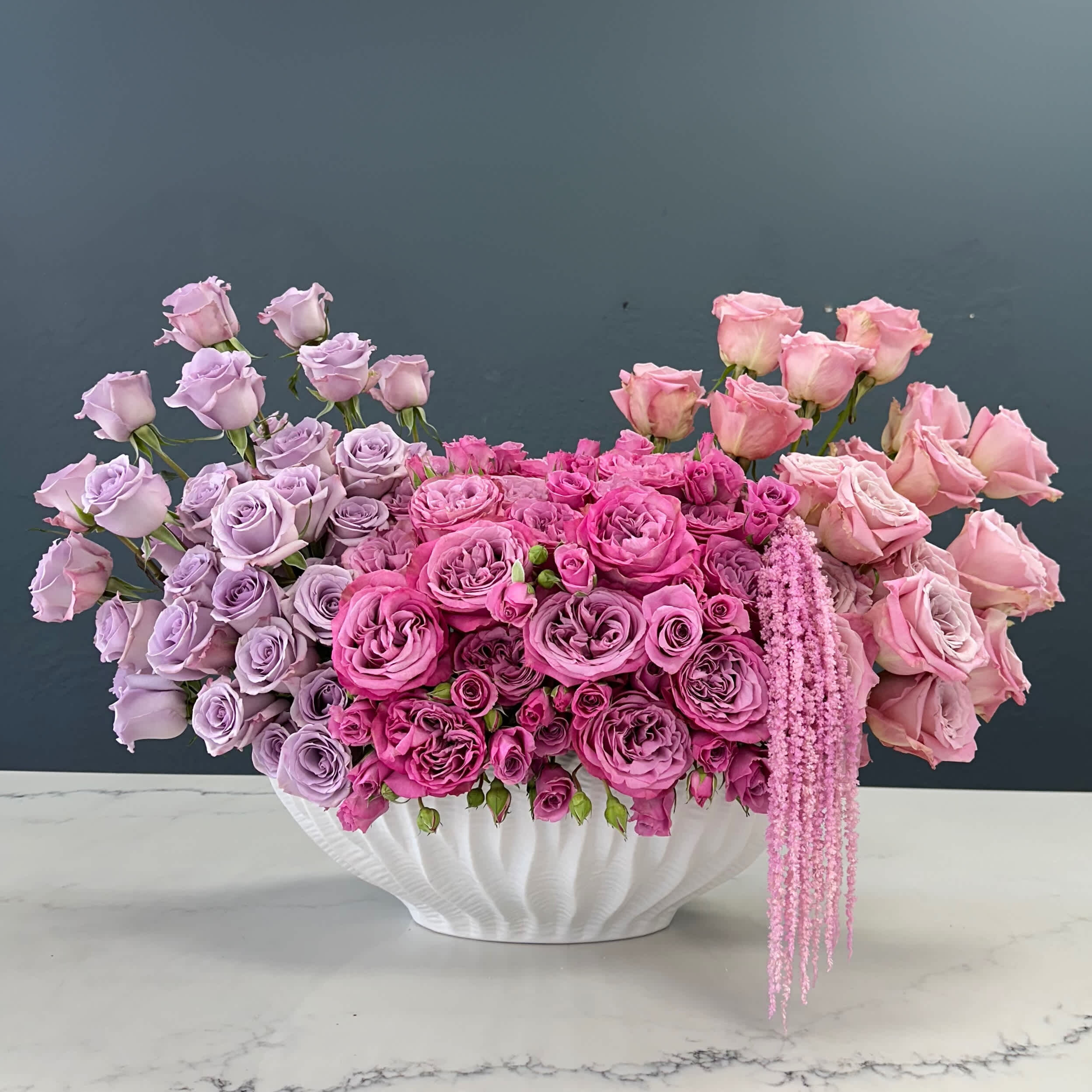 Queen Elizabeth Queen Elizabeth - Components: Ivory Roses: Soft and creamy ivory roses form the base of the arrangement, providing a lush and romantic feel. Coffee-Colored Roses: These roses add depth and contrast with their rich, warm tones, creating a captivating visual interest. Coffee Orchids: Delicate coffee orchids interspersed among the roses introduce a unique texture and an exotic touch. Design: Shape: The arrangement is designed in a classic, symmetrical shape, allowing the beauty of each flower to be showcased. Height and Balance: Varying heights of the flowers add dimension, with the tallest flowers centrally placed, gradually tapering down towards the edges. Placement: The ivory roses are evenly distributed, while the coffee-colored roses are strategically positioned to draw the eye. The coffee orchids are nestled amongst the roses, peeking out to provide a delightful surprise element. Vase: Material: The vase is crafted from fine ceramic with a glossy white finish. Shape: Its clean lines and simple silhouette serve as the perfect backdrop, highlighting the vibrant colors and natural beauty of the flowers. Visual Appeal: Color Palette: The neutral ivory and coffee tones create a serene and sophisticated palette, suitable for any elegant setting. Texture: The smooth petals of the roses contrast beautifully with the slightly more textured orchids, adding depth and interest. Ideal Settings: This arrangement is perfect for: Home Décor: Adding a touch of elegance to living rooms, dining tables, or entryways. Special Occasions: Enhancing the ambiance of weddings, anniversaries, or intimate dinner parties. Corporate Spaces: Bringing a refined and welcoming atmosphere to office lobbies or meeting rooms. This ivory and coffee floral arrangement, with its understated yet luxurious design, is sure to elevate any space with its timeless beauty and sophisticated charm. Specialty roses of pink, purple and fucsia gathered in a white vase description 3/3 ChatGPT Vibrant Specialty Rose Arrangement This stunning floral arrangement features an exquisite selection of specialty roses in shades of pink, purple, and fuchsia, artfully gathered in a sleek white vase. The vivid hues and elegant design create a striking visual display, perfect for adding a touch of luxury and vibrancy to any space. Components: Pink Roses: Soft and romantic, the pink roses add a gentle and sweet touch to the arrangement. Purple Roses: These roses introduce a sense of mystery and elegance with their deep, rich tones. Fuchsia Roses: Bright and bold, fuchsia roses inject energy and a pop of color, making the arrangement truly stand out. Design: Shape: The arrangement is crafted in a rounded, dome shape, providing a lush and full appearance. Height and Balance: The flowers are arranged in a balanced manner, with the tallest blooms at the center, gradually tapering down towards the edges to create a harmonious and cohesive look. Placement: Pink roses are distributed evenly throughout the arrangement, while purple and fuchsia roses are strategically placed to create dynamic bursts of color. Vase: Material: The vase is made of high-quality ceramic, with a smooth and glossy white finish. Shape: Its simple, cylindrical shape provides a contemporary and elegant foundation that highlights the vibrant colors of the roses. Visual Appeal: Color Palette: The combination of pink, purple, and fuchsia creates a lively and captivating palette, perfect for adding a splash of color to any setting. Texture: The smooth, velvety petals of the roses provide a rich and luxurious texture that enhances the overall visual appeal.