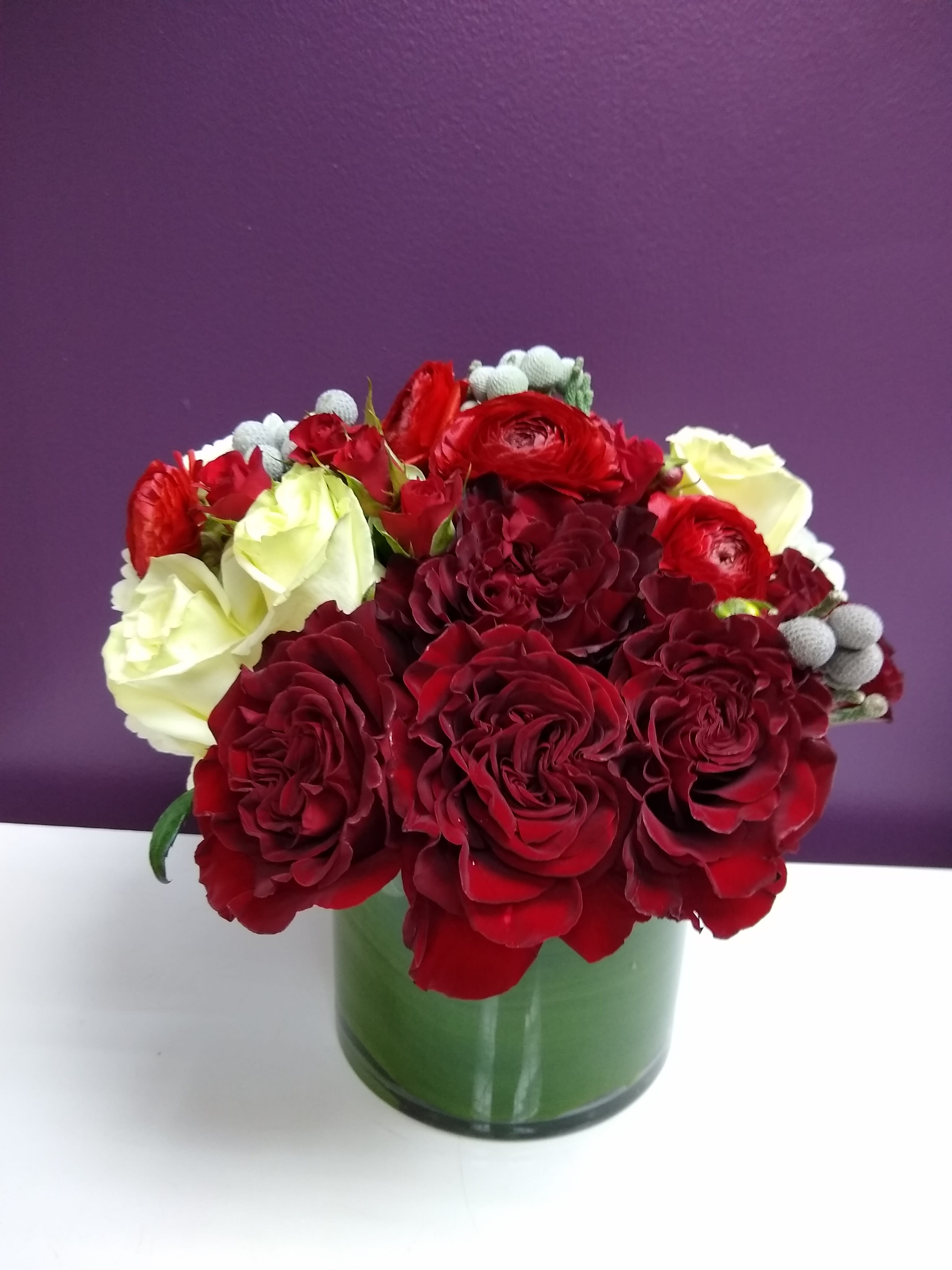 Stunning Red - Stunning Red Roses are accented with Silver Brunia Balls, white roses, white hydrangeas and red ranunculus.   6x6 glass vase.