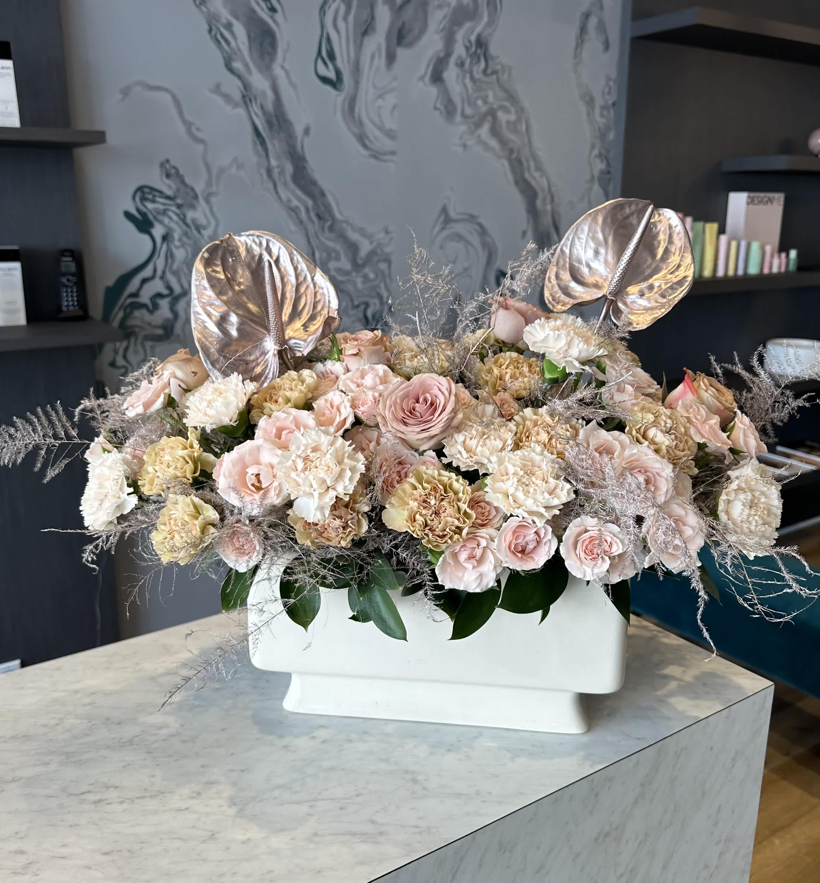 Cream  arrangement  - This exquisite cream-colored vase showcases a stunning arrangement of flowers, artfully combining the classic beauty of roses, the vibrant charm of carnations, and the exotic elegance of anthuriums. The roses, in their various shades, add a touch of timeless romance, while the carnations contribute a splash of cheerful color. The anthuriums, with their unique shape and glossy appearance, bring an exotic flair, making this floral composition a captivating centerpiece. The cream vase, with its subtle and sophisticated hue, perfectly complements the vivid blooms, creating a harmonious and elegant display that will enhance any room.