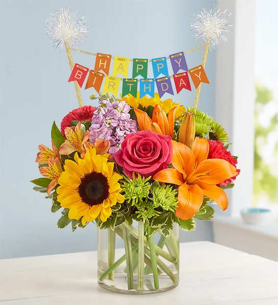 Floral Embrace with Happy Birthday Banner - Like a warm embrace, our vibrant flower bouquet delivers your birthday wishes to someone special. A rich gathering of yellow and orange blooms, with pops of bright pink and purple, it's bundled with our exclusive banner, adding color and sparkle to their celebration.