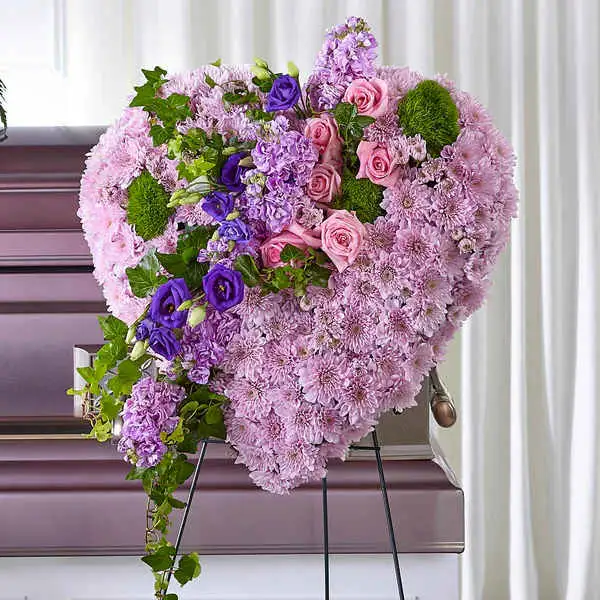 Treasured Love Standing Heart - For those who you will always hold close to your heart, share your sympathies with our Treasured Love Standing Heart. This beautiful display is a thoughtful take on a traditional heart and is crafted with cushion pompons, roses, lisianthus and stock
