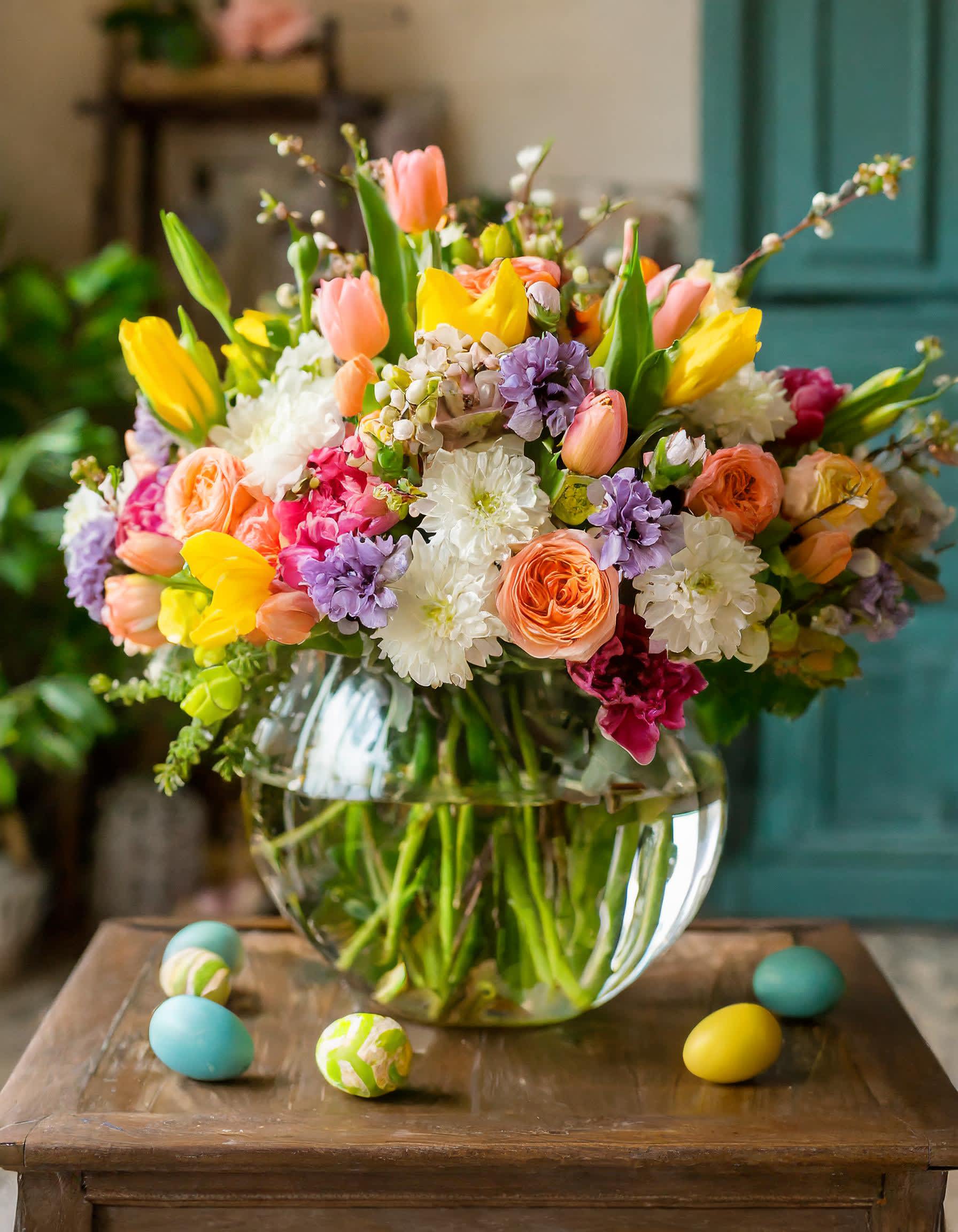 Easter Blossom  - A clear vase with Easter's vibrant essence, a garden-style symphony in white dahlia, yellow tulips, peach roses. It's a masterpiece of natural abundance and elegance, evoking the beauty of a sun-kissed garden in full bloom. 