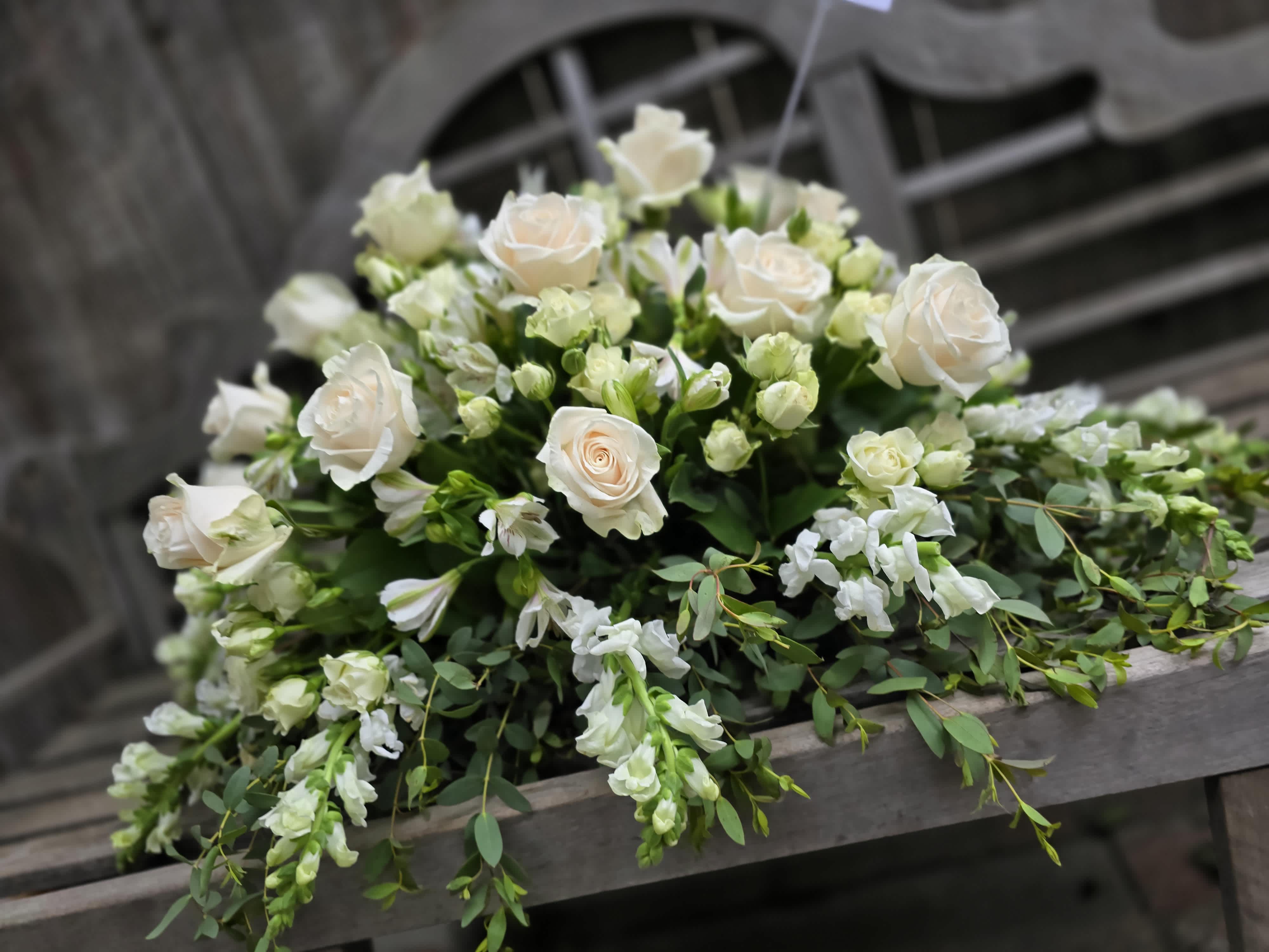 Dearest memories white casket spray - A beautiful all white and simple design in the classic all white. Casket spray featuring white roses, spray roses. Snap dragons, and alstroemaria.