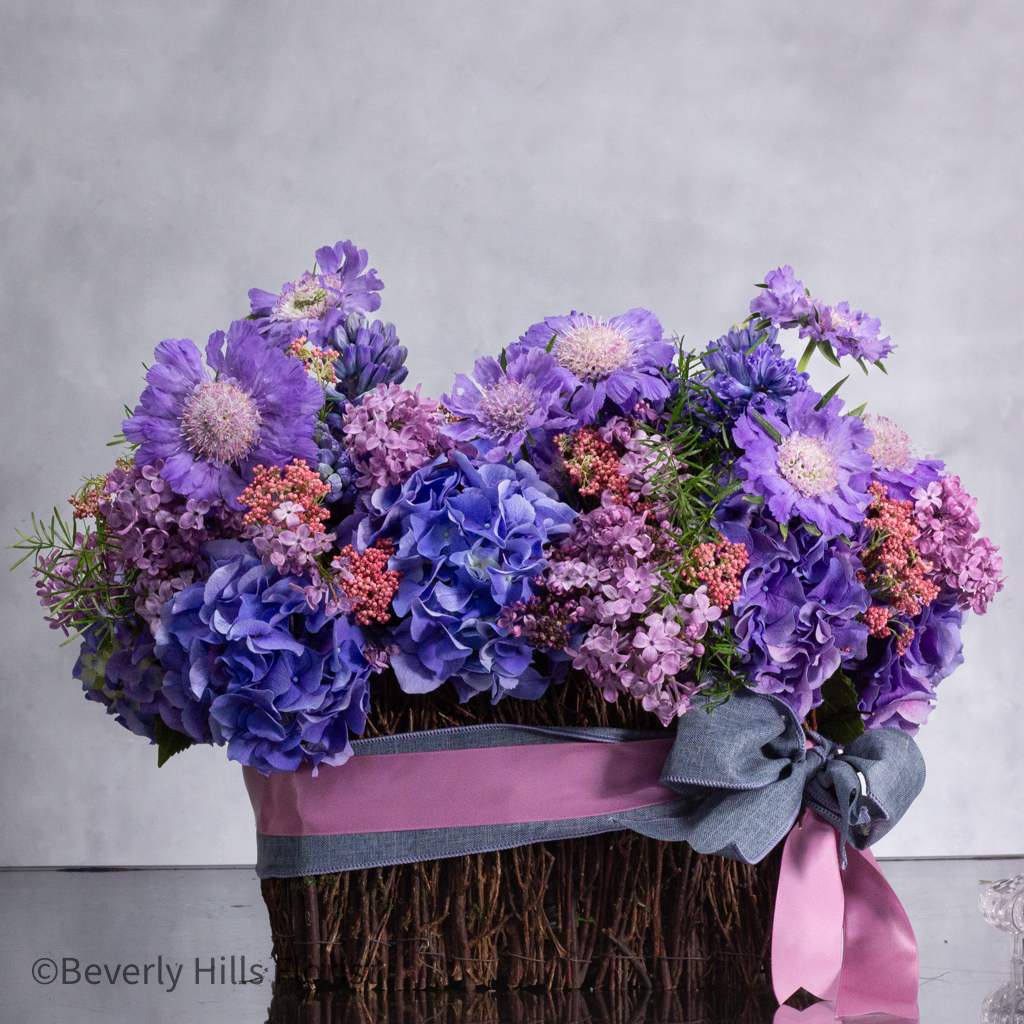 Hyacinth Heights - Pasadena Florist - Same Day Delivery in Los Angeles, Beverly Hills, and surrounding areas. Order Now with Beverly Hills Florist.  Imagine a woven basket brimming with a delightful array of blooms in shades of lilac, hydrangea, and lavender, accentuated by subtle touches of blue. This enchanting arrangement features fragrant hyacinths, delicate lilac blooms, and lush hydrangeas, creating a captivating display of color and texture. Perfect for expressing your admiration or sending well wishes, this basket arrangement is available for same-day delivery, ensuring your heartfelt sentiments are conveyed with beauty and grace. Approx.: 15 Long and 10&quot; tall  