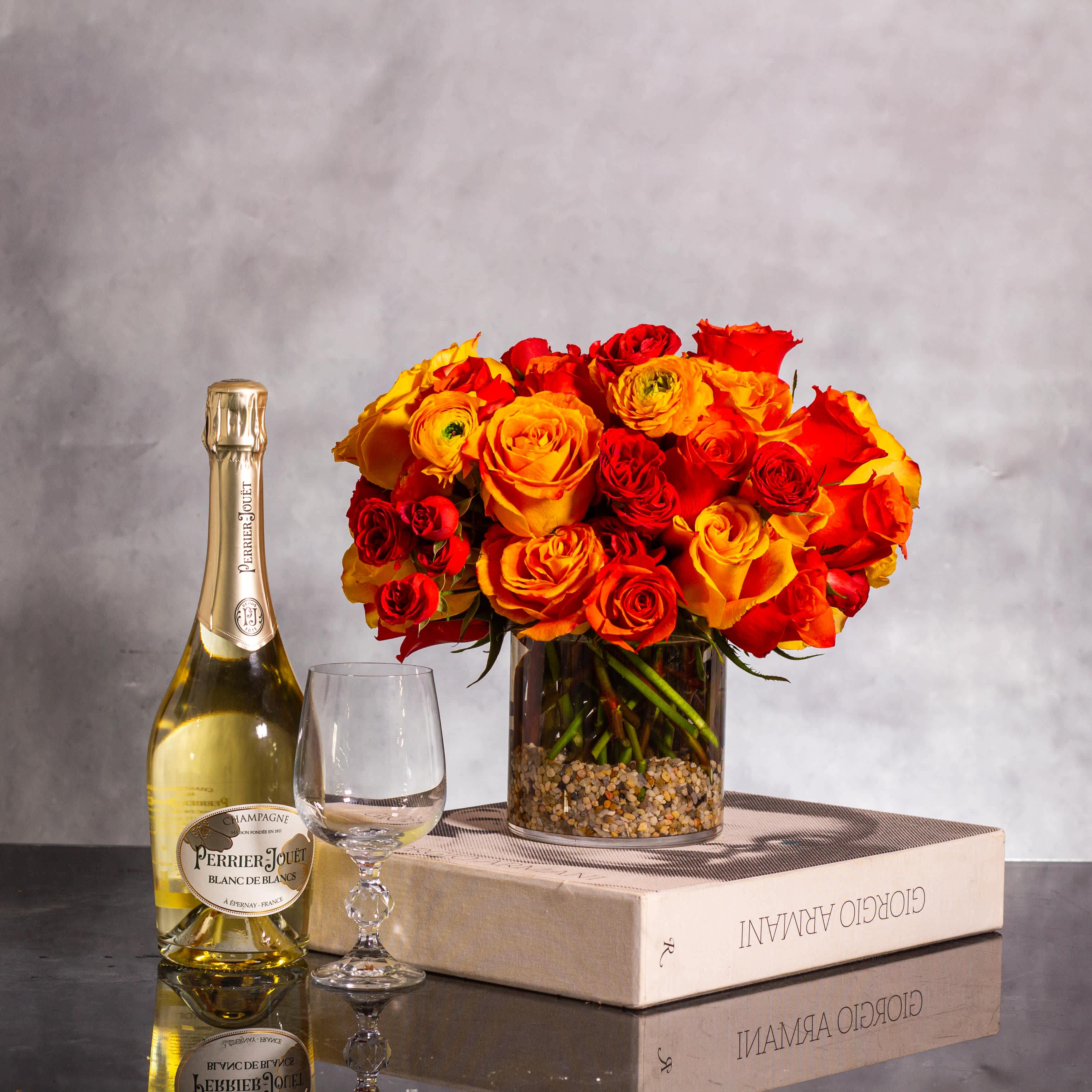 Sun-Kissed Splendor - Accidental Elegance Floral Arrangement - Pasadena Florist - Crafting a stunning floral arrangement in a 5x5 cylinder vase with an accidental rock inclusion, exposed rose stems, over 25 stems of roses, and clusters of rinocular blooms in bright orange and yellow shades, here is a descriptive representation:  &quot;Introducing our Accident with Rocks arrangement, where beauty meets the unexpected. Delight in the sight of beautiful rose stems artistically displayed in a 5x5 cylinder vase, with over 25 radiant roses standing tall alongside charming rinocular blooms in vivid shades of orange and yellow. This happy union of spray roses and classic roses creates a jubilant atmosphere, exuding cheer and vibrancy. With an overall height and width of 10 inches by 10 inches, this arrangement is a harmonious blend of nature and spontaneity, perfect for brightening any space with its unique charm.&quot;