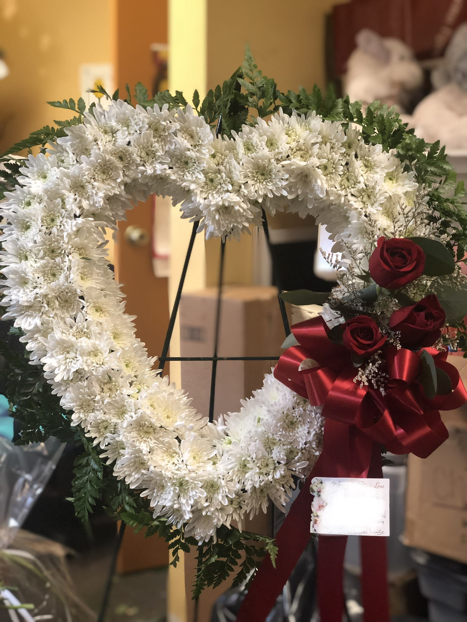 Pure of Heart Spray - An 18&quot; heart  with three red roses and greens set admist a bed of  white maisy mums,.