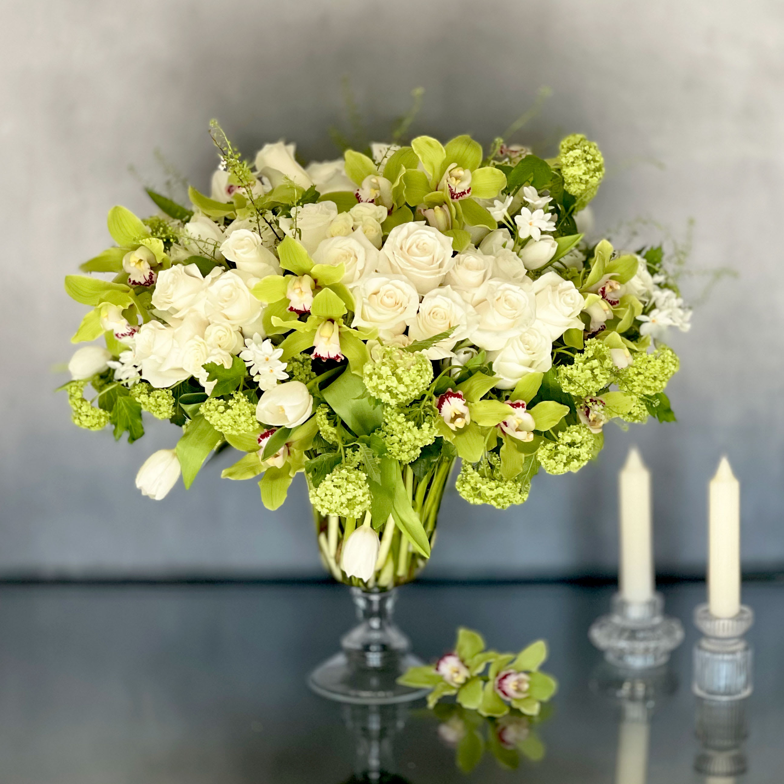 Roman Holiday - Pasadena Florist - Delicate, charming, and always a favorite. Our Roman Holiday bouquet features a mix of 50 white roses, 20 tulips, Vibernum and 18 Cymbidium orchids and seasonal greens in a glass pedestal vase.This arrangement has been picked fresh for you to help you celebrate a birthday, anniversary, or convey your message of love and sweet affection.  Measurement:   about 20&quot; Tall and 25&quot; wide 