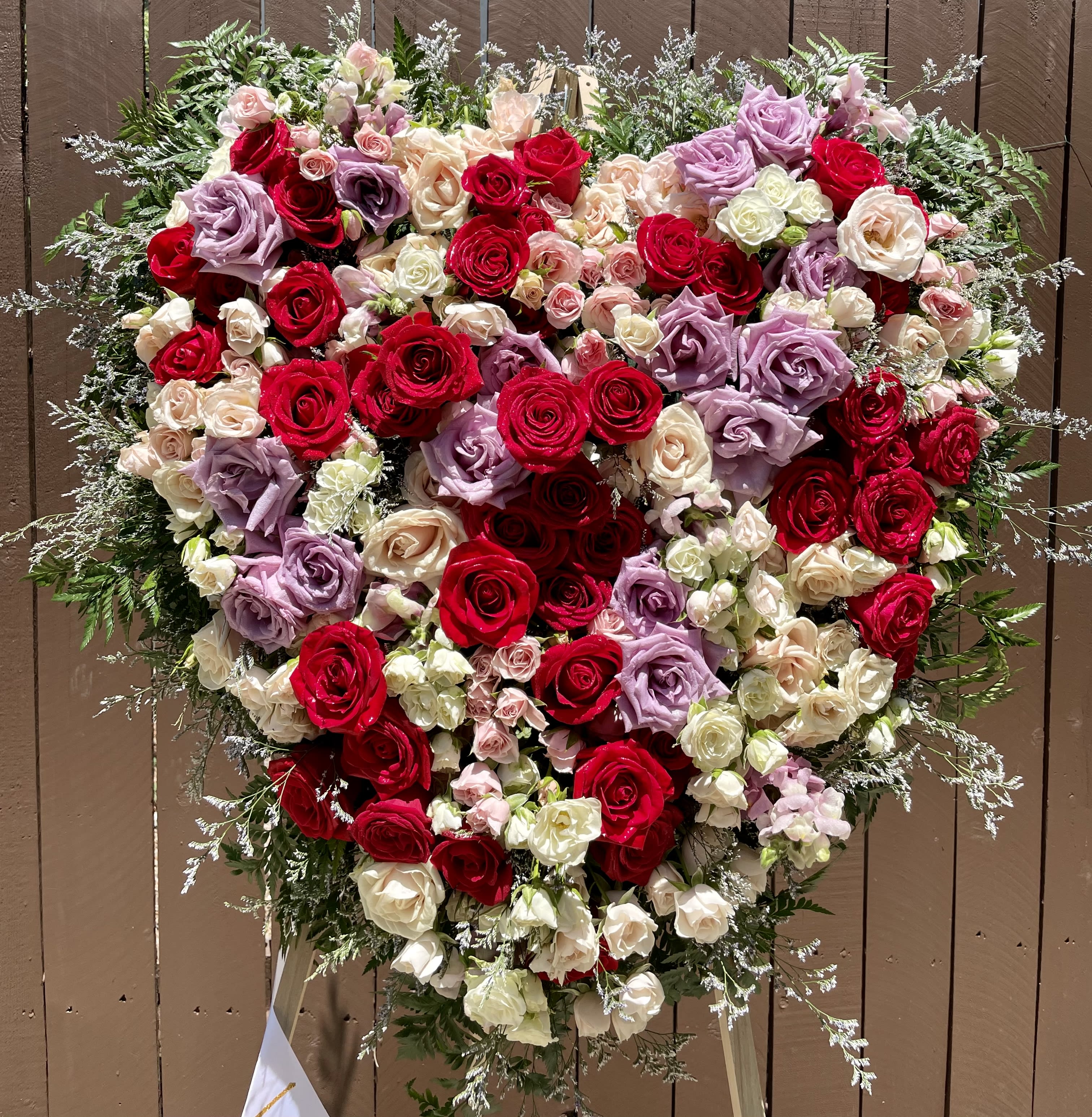 Heart Full of Roses  - Full Heart designed in a mixture of lush roses and spray roses in reds, blushes and ivories. The perfect selection to celebrate your loved one.   Our designs are sure to stand out as each arrangement is carefully created to capture the emotion with flowers. Arrangement comes with easel and ribbon with your choice of writing. 