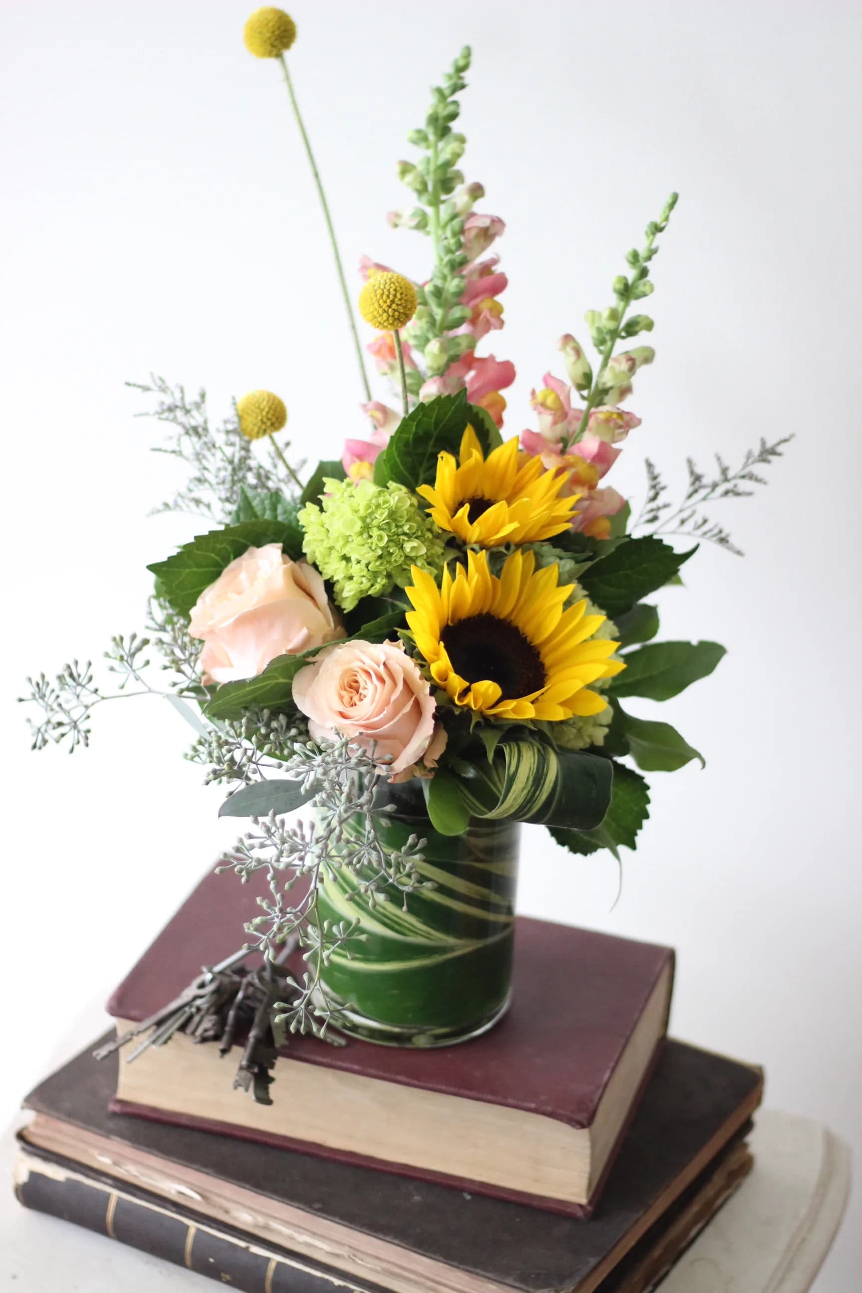 Let the Sunshine In - This collection of sunflowers, roses, seasonal accents and whimsical craspedia is sure to lift the spirits on an otherwise rainy day or the perfect gift on a happier occasion. 