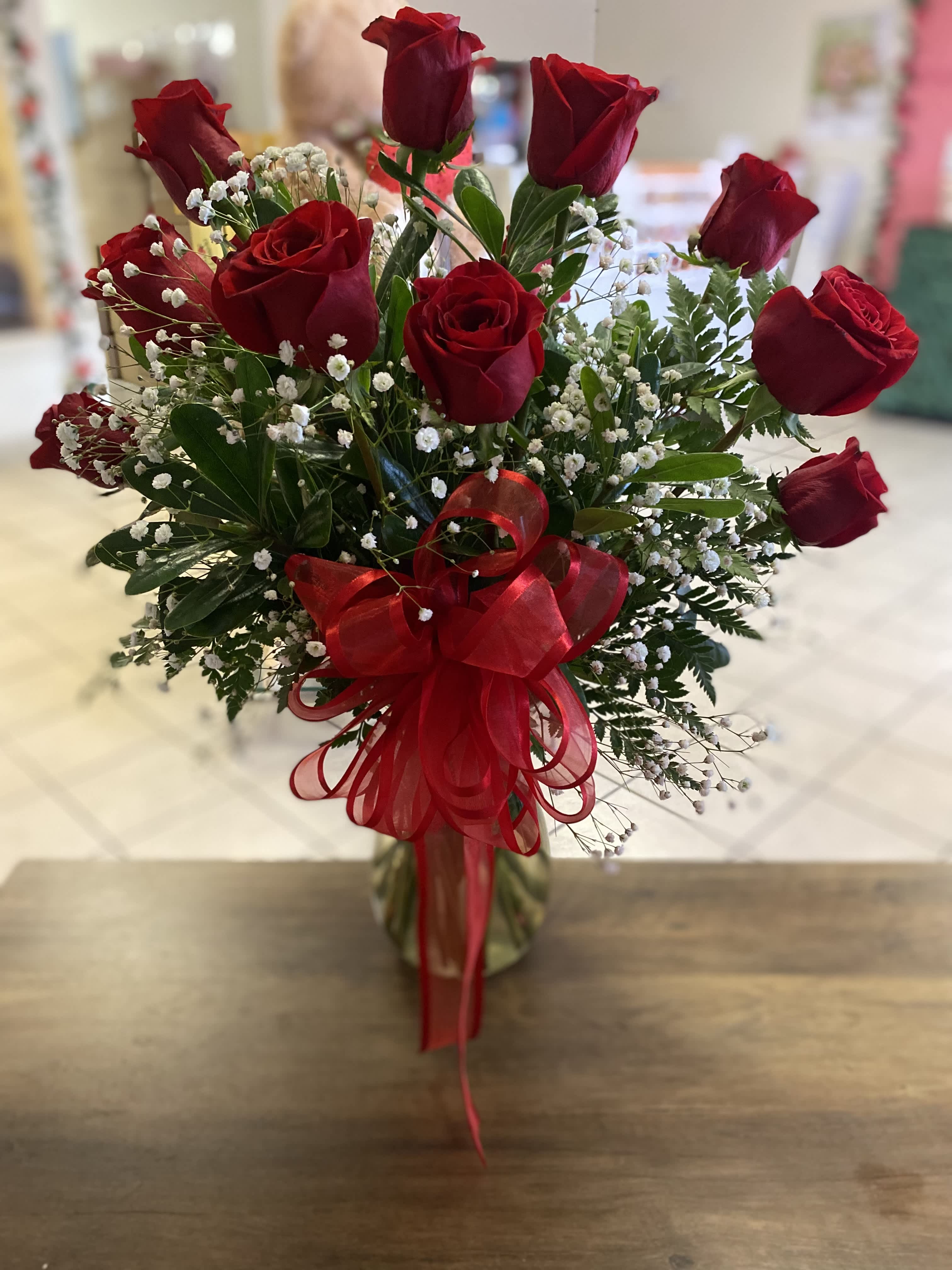 One Doz Red Roses in an arrangement One Doz Red Roses in an arrangement - Twelve beautiful red roses arranged in a vase with baby’s breath. Topped off with a red ribbon