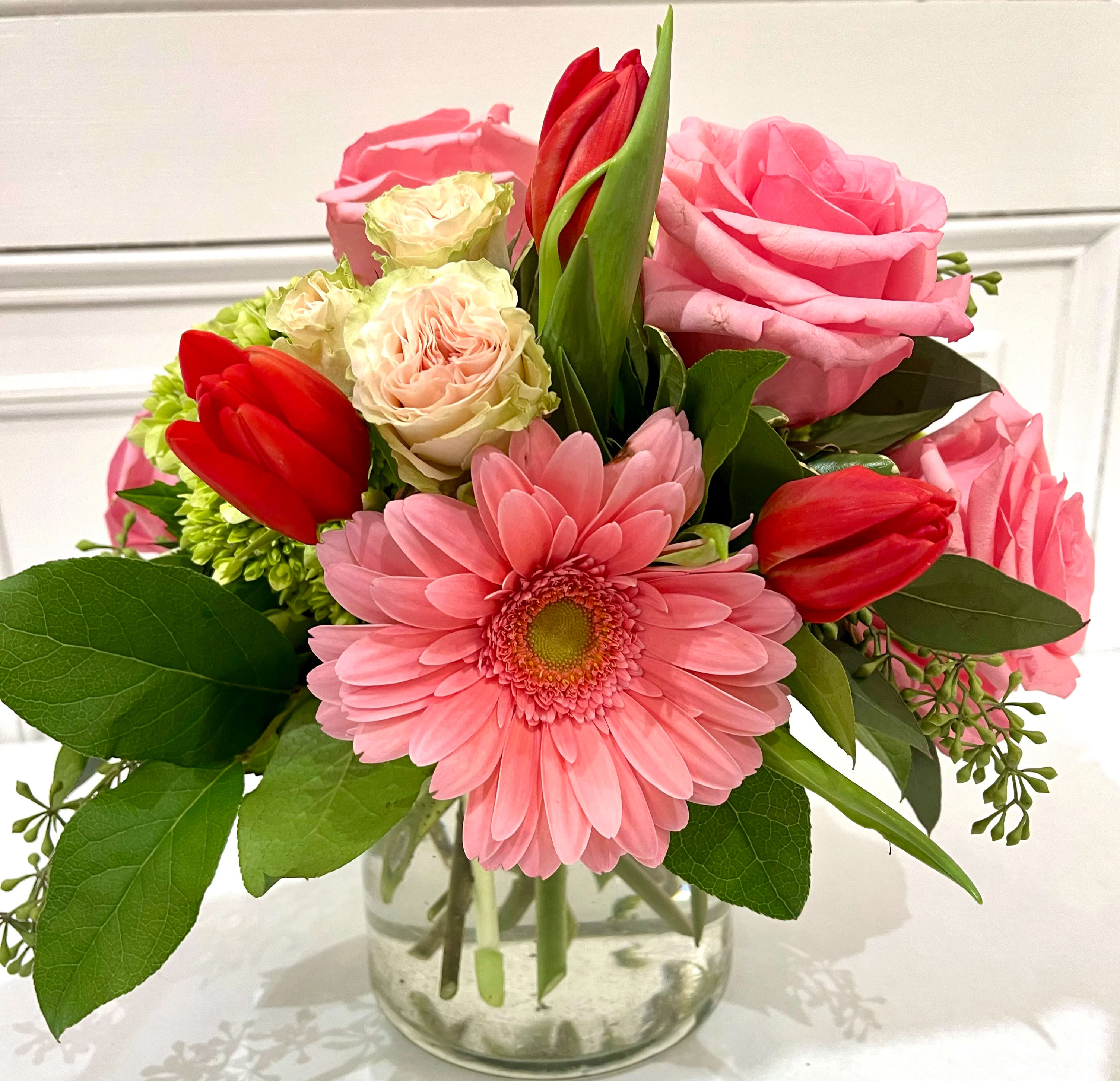 "Pretty & Sweet" Bouquet "Pretty & Sweet" Bouquet - Pink roses, gerbs, and spray roses are contrasted against red tulips and green hydrangea. As tulips are seasonal, there may be a necessary red floral substitution. Arranged in a small cylinder, it's a perfect token of your affection.