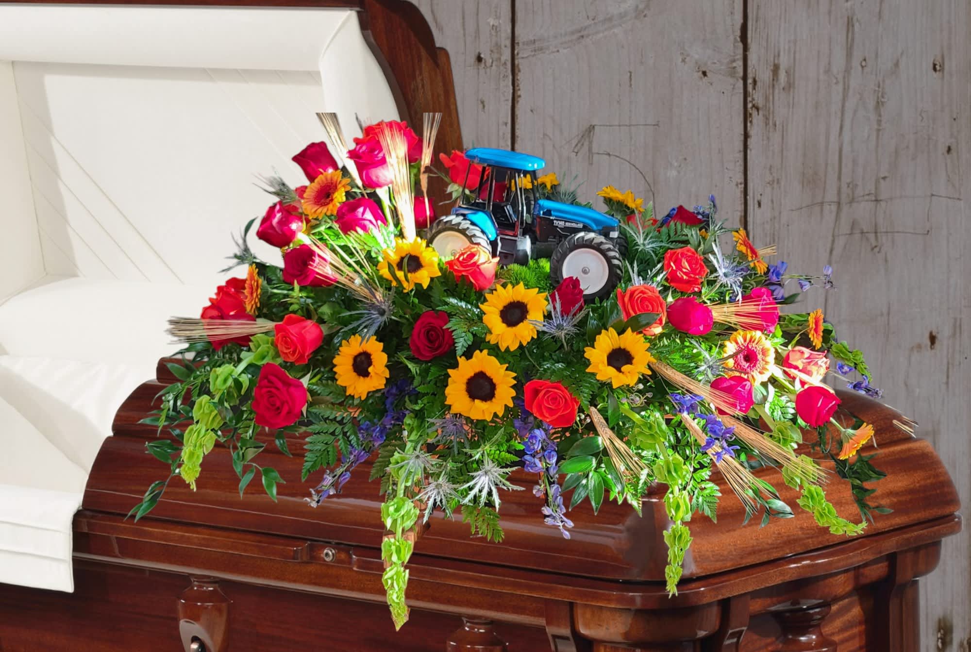Harvest Spray Harvest Spray - His Passion was farming. The half couch Harvest Spray is a wonderful tribute to the farmer in your life. Filled with Red roses, Sunflowers, Wheat, Blue Delphinium, Eringium, Bells of Ireland, and Gerbera Daisies, this spray is full of texture, color, and beauty. Tractor is supplied by the family and the spray can be customized to any brand preference (J.D., Ford, IH, Kubota, Etc)