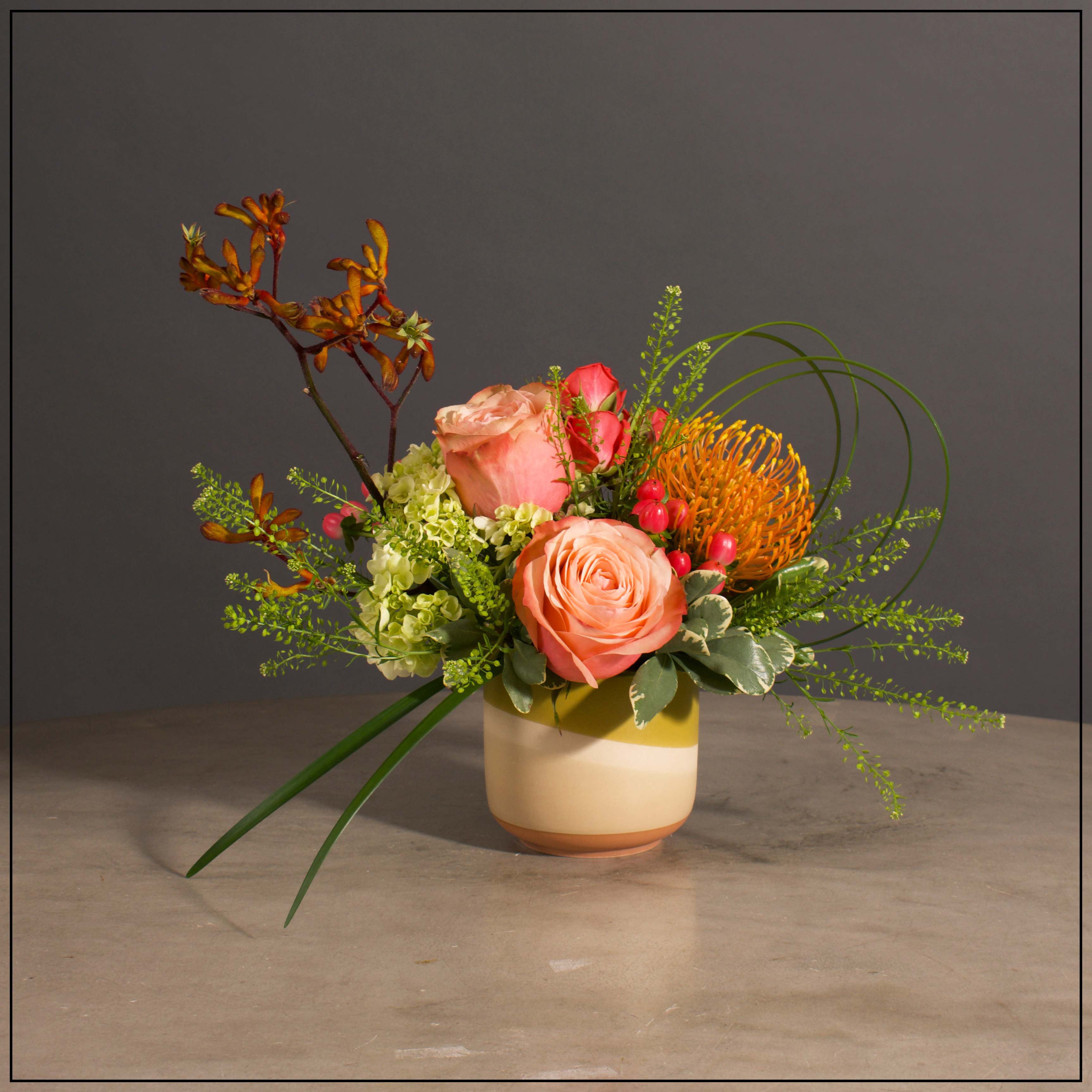 Sunset - Roses, Spray Roses, Protea and Kangaroo Paw with Filler and Greens in a Cute Ceramic Pot.  Approximately 11&quot; H x 11&quot; W
