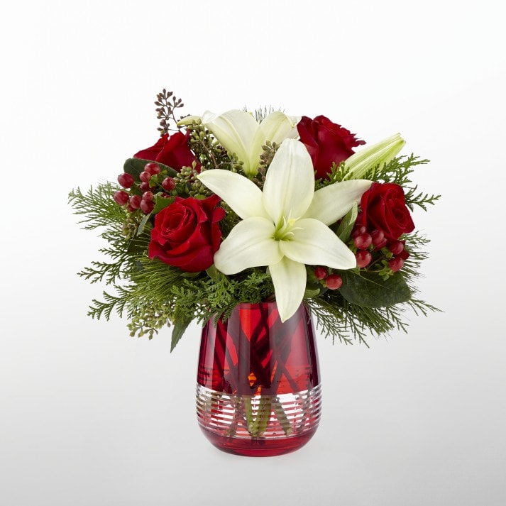 The FTD® Festive Holiday™ Bouquet by Vera Wang - FTD® proudly presents the Festive Holiday™ Bouquet by Vera Wang. Blooming with the glamour and elegance of this festive holiday season, this stunning Christmas bouquet has been conceived of by none other than style icon Vera Wang. White Asiatic Lilies pop against a crimson background of rich red roses, beautifully accented with red hypericum berries, seeded eucalyptus, and an assortment of fragrant holiday greens. Presented in a chic and modern red glass vase with a striped, clear embellishment at the bottom, this fresh flower bouquet has been created just for you to send your warmest season's greetings in style.   Container is discontinued, we will sub in a similar container