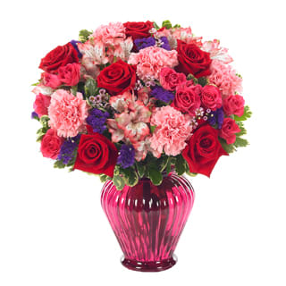Ever-Budding Romance - Product ID: BF111-11KM  Love is in full bloom as red roses, lavender waxflower, pink and white alstroemeria, hot pink spray roses, purple statice and pink carnations converge romantically in a pretty red vase. Measures 17âH by 14âL