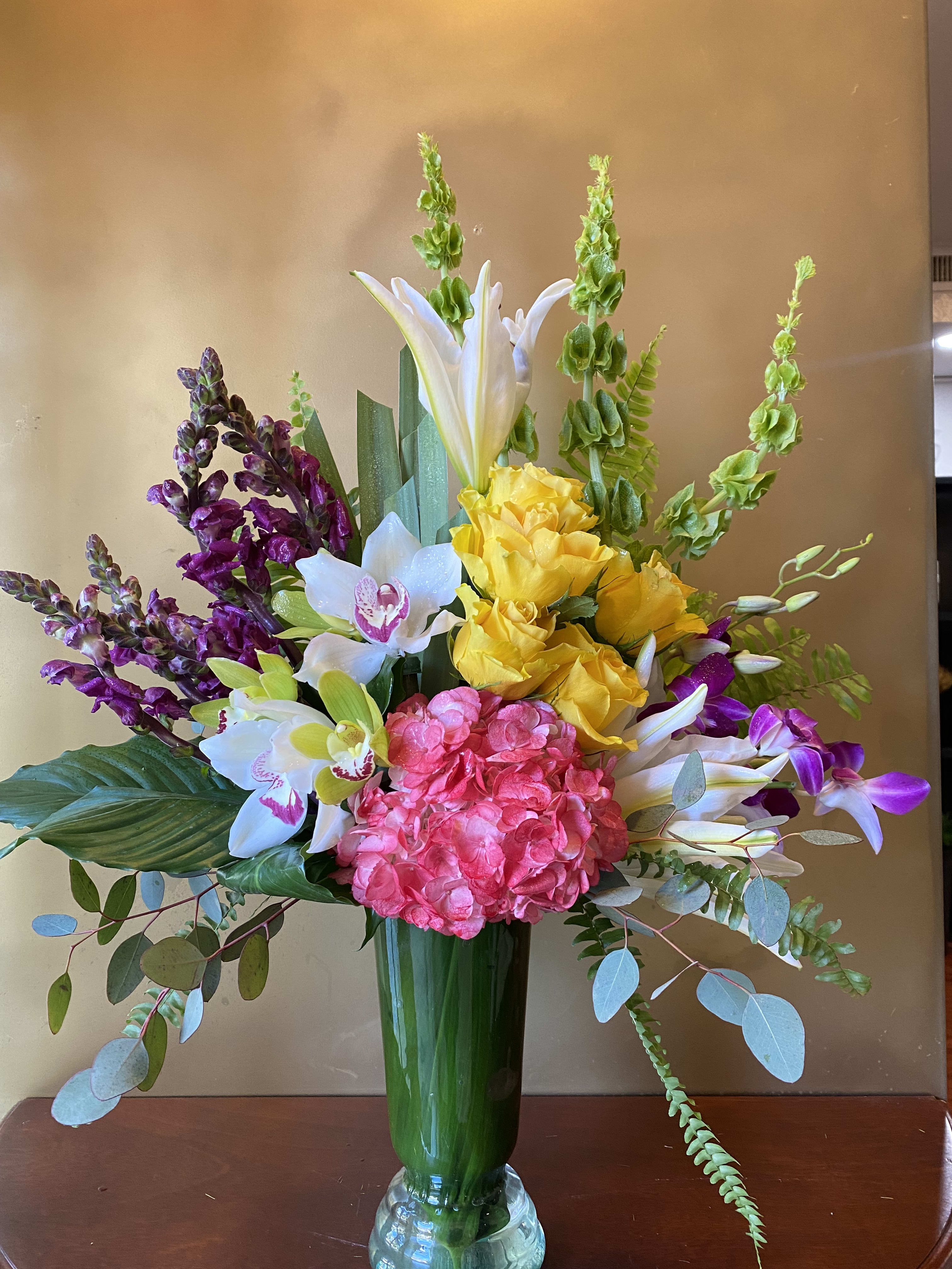 Pretty Paradise - Send that special someone on a trip to paradise, no plane tickets required! This magical mix of luxurious pink, yellow and green blooms bursts with color, texture and personality. It's a tropical treat they'll never forget! This pretty bouquet features dark pink hydrangea, green cymbidium orchids, yellow mokara orchids, yellow roses, hot pink oriental lilies, orange snapdragons, bells of Ireland, hanging green amaranthus, huckleberry, sword fern, Ti leaves, ti leaves, bear grass, and lemon leaf. Delivered in a clear glass vase.