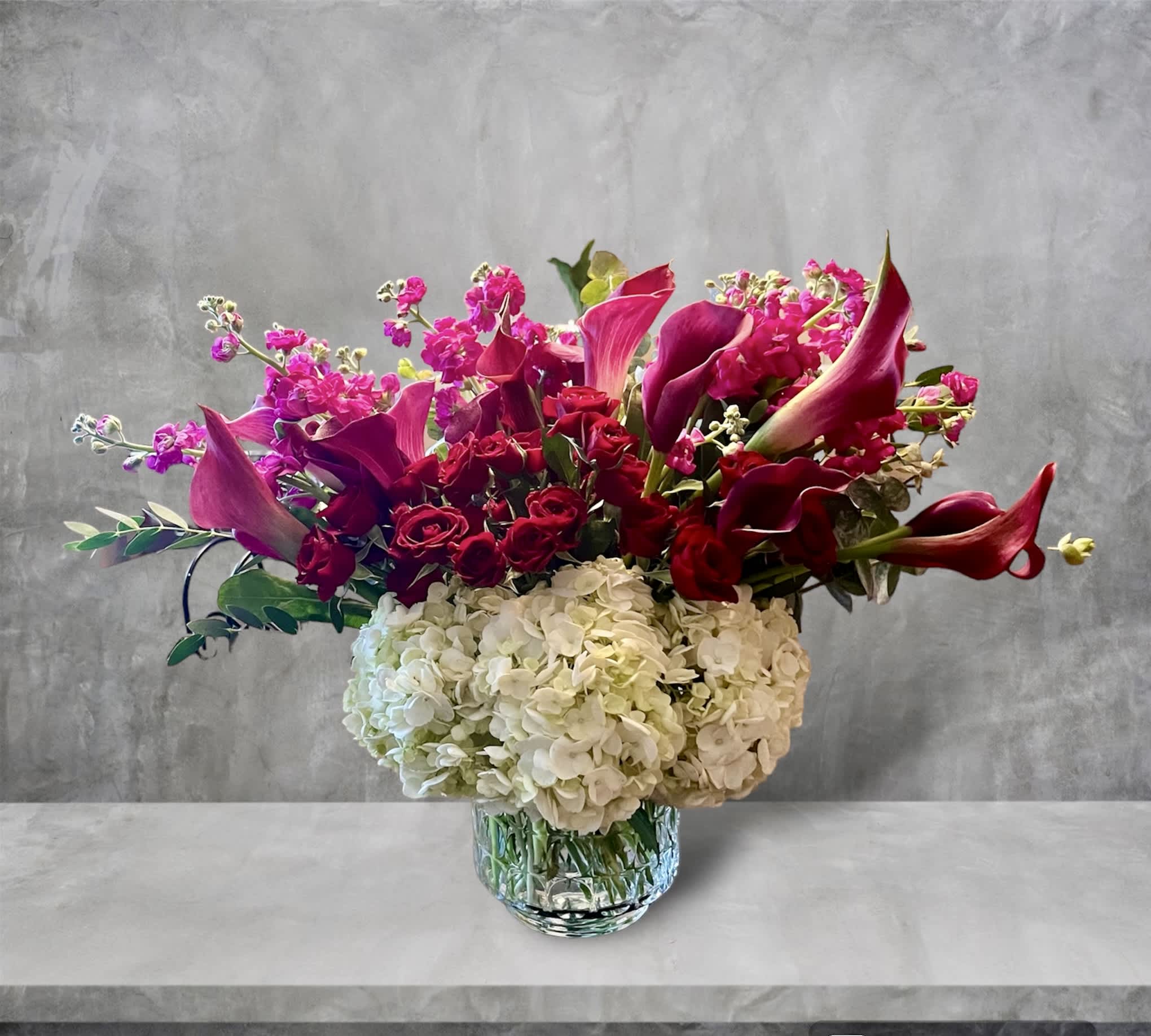Classy Calla's Classy Calla's - A romantic mix of purple and red featuring mini calla lilies, spray roses, hydrangea, stock and eucalyptus in a decorative glass vase. A perfect Anniversary, Valentine, or everyday gift.