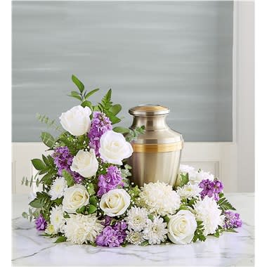 Cremation Wreath- Lavender And White - Honor their memory and celebrate the joy they brought to their loved ones. Our elegant wreath arrangement is handcrafted from a soothing mix of blooms, creating a peaceful tribute, while offering comfort during a difficult time. All-around asymmetrical wreath arrangement of white roses, football mums and cushion poms, lavender stock; accented with baby’s breath and assorted greenery Intended to be sent to the memorial service; urn or framed photograph can be placed in the center of the wreath Large arrangement measures approximately 19&quot;H x 21&quot;W Small arrangement measures approximately 17&quot;H x 19&quot;W Our florists hand design each arrangement, so colors and varieties may vary due to local availability