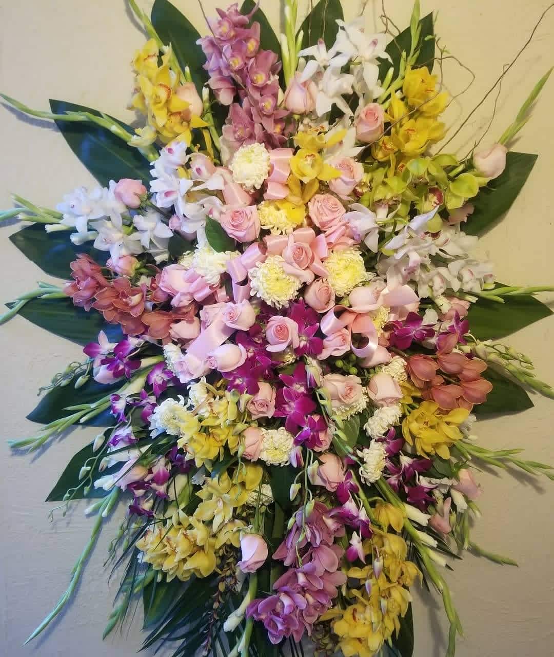 Orchids Delicacy - Standing funeral spray with yellows pinks purples  Colors can be modified per request. Florist may substitute based on availability.