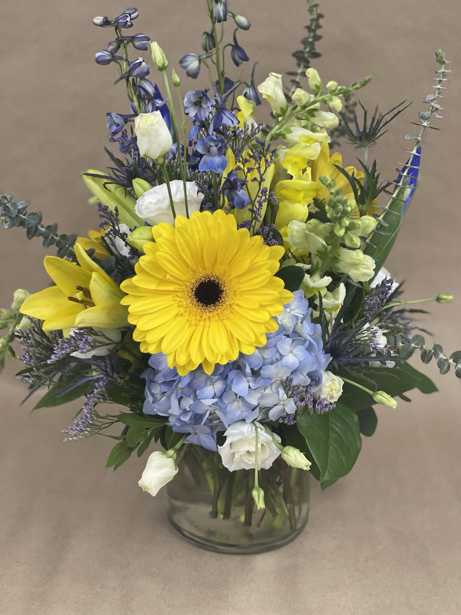Sunny Skies Sunny Skies - Yellow, White,and Blue Seasonal Flowers in a glass container. A bright a cheerful arrangement for all occasions.