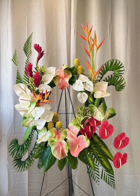 Aloha Homage - Aloha Homage, an exquisite tribute designed to convey heartfelt condolences and honor the memory of a loved one. This elegant wreath features a harmonious blend of anthuriums in serene shades of pink, red, and white, accompanied by graceful heliconia and delicate ginger blooms. Lush ferns and tropical leaves create a soothing, natural backdrop, enhancing the wreath's tranquil beauty.  Perfect for funeral services or memorial gatherings, our Aloha Homage is meticulously handcrafted to offer comfort and convey deep respect. Let this beautiful floral design serve as a poignant reminder of the vibrant and cherished life of the loved one, bringing a touch of tropical peace and solace during a difficult time.  24&quot; wreath base. Easel included.  ***May require minimum of three days notice***