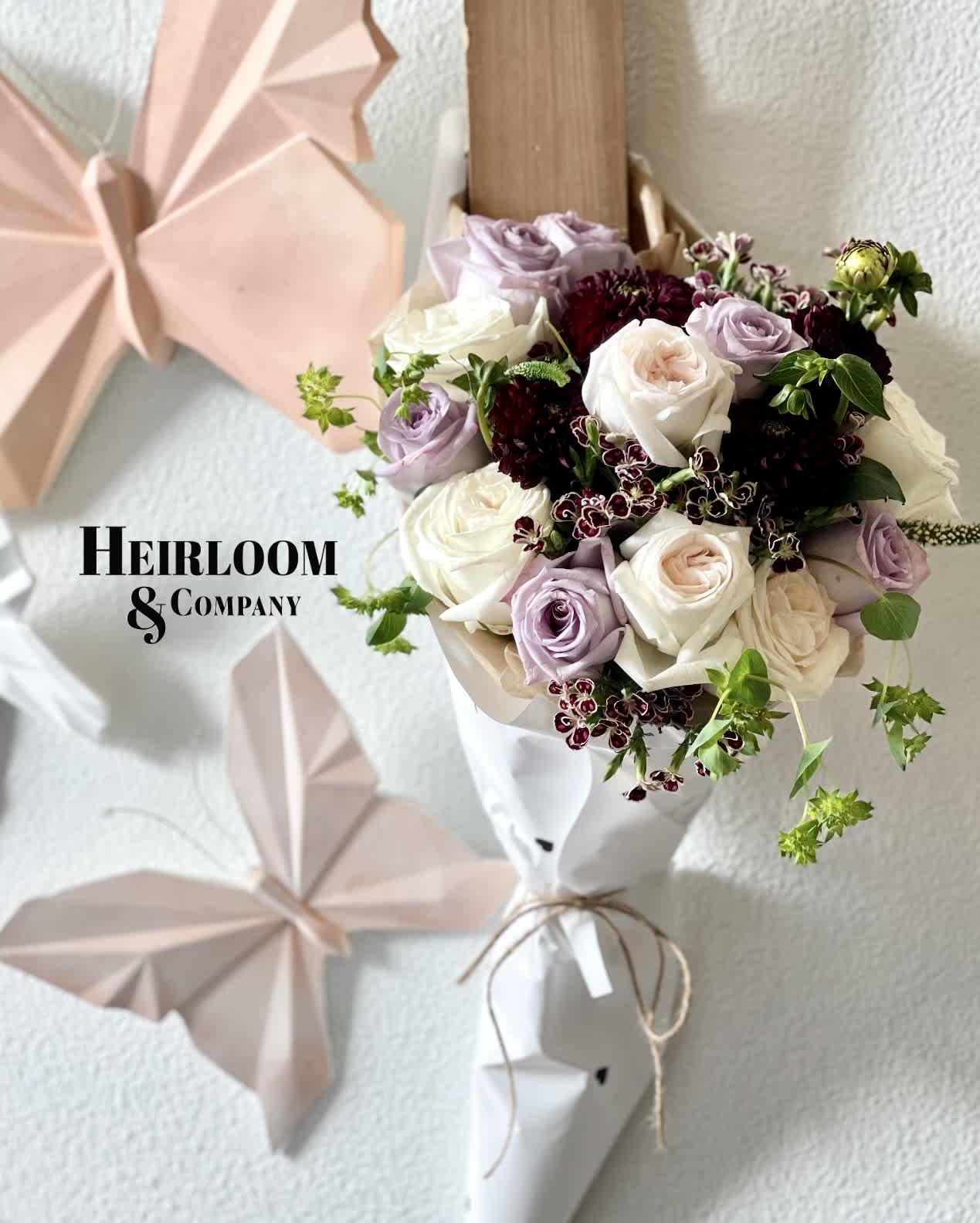 Lavender Haze - A hand held bouquet filled with our most stunning purple roses, deep purple dahlias, purple and white carnations, and are most premium hand-picked garden roses in the largest of blooms. Wrapped with an adorable white wrap with mini Black hearts printed on it. Tied together with an oversized twine bow.