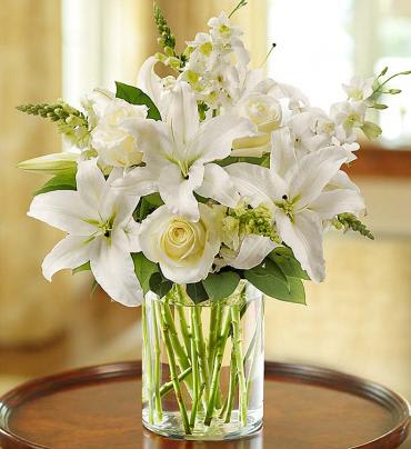 Classic All-White Arrangement Classic All-White Arrangement - Glorious roses lead the way in this luxurious winter white arrangement. Paired with lilies, orchids, snapdragons and salal, they're hand-gathered in a stylish cylinder vase to evoke an evening stroll at the heart of the season.