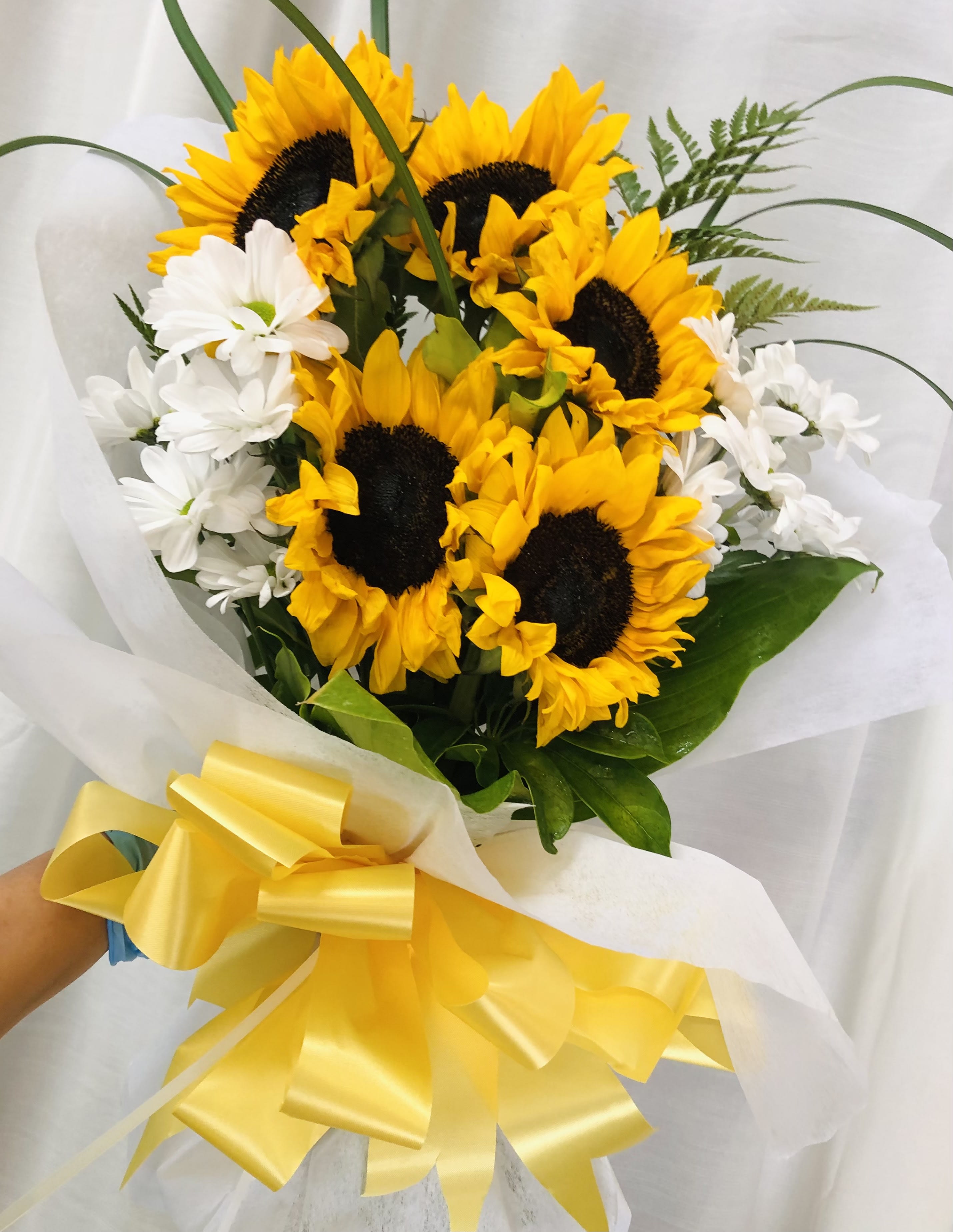 Breeze Of Sunshine - Vibrant bouquet of yellow, and white flowers with green accents wrapped in white with yellow ribbon.  Featuring sunflowers, daisies, and leaf accents.