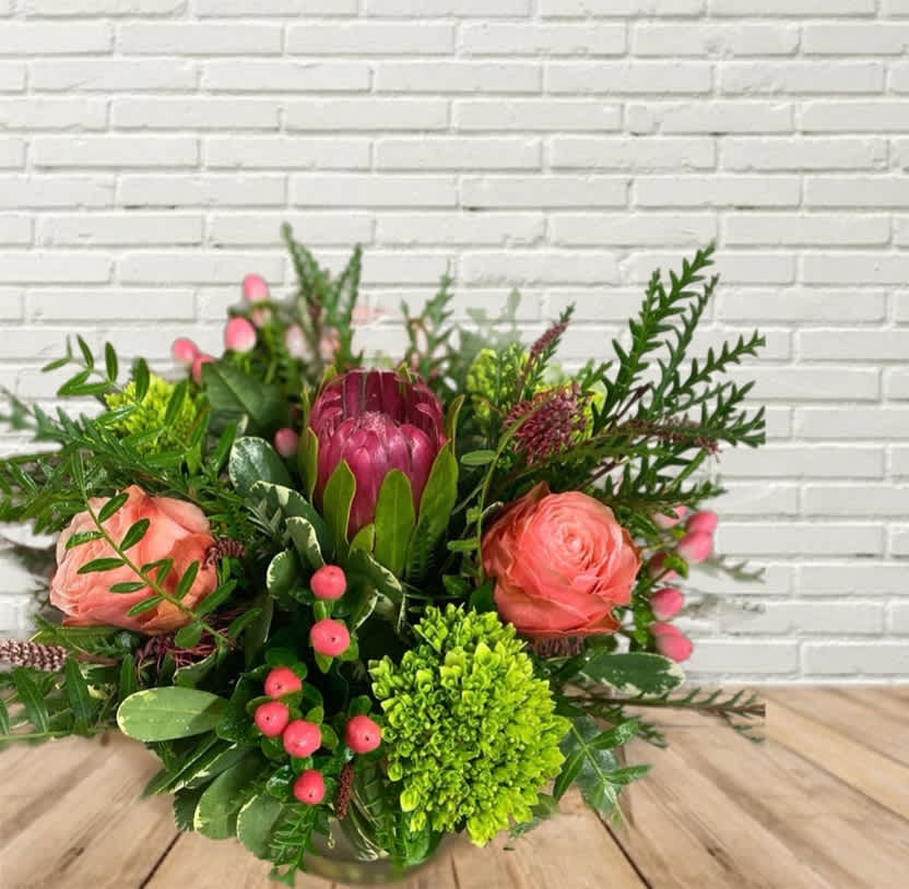 Queen Protea Queen Protea - A low & lush protea featured arrangement with mini green hydrangeas, peachy roses, and hypericum with seasonal greens!